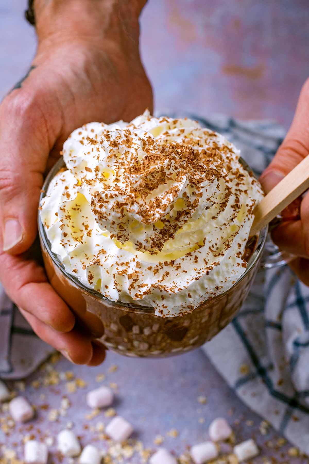 A pair of hands holding a mug of cream topped hot chocolate.