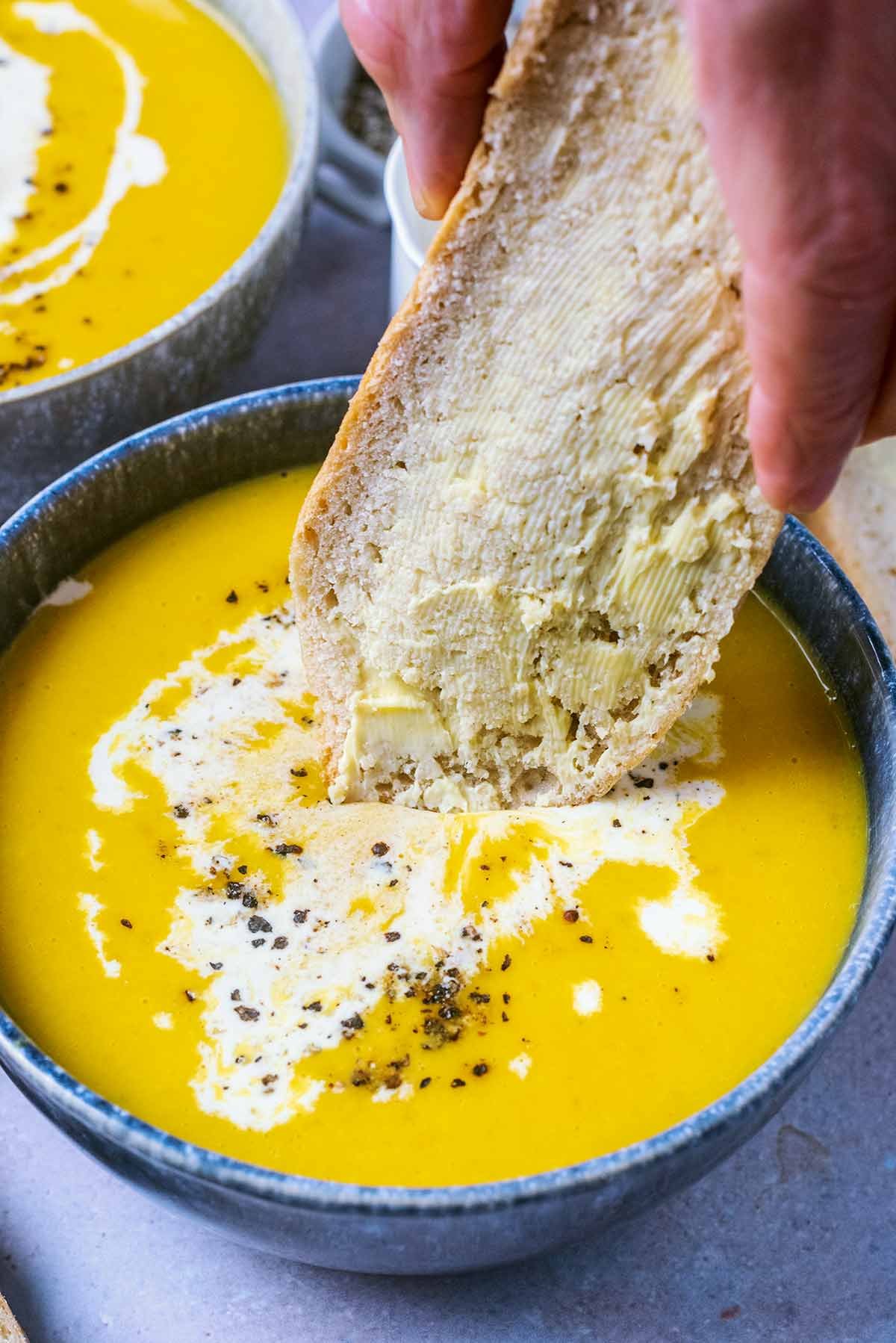 A slice of buttered bread being dipped into a bowl of creamy soup.