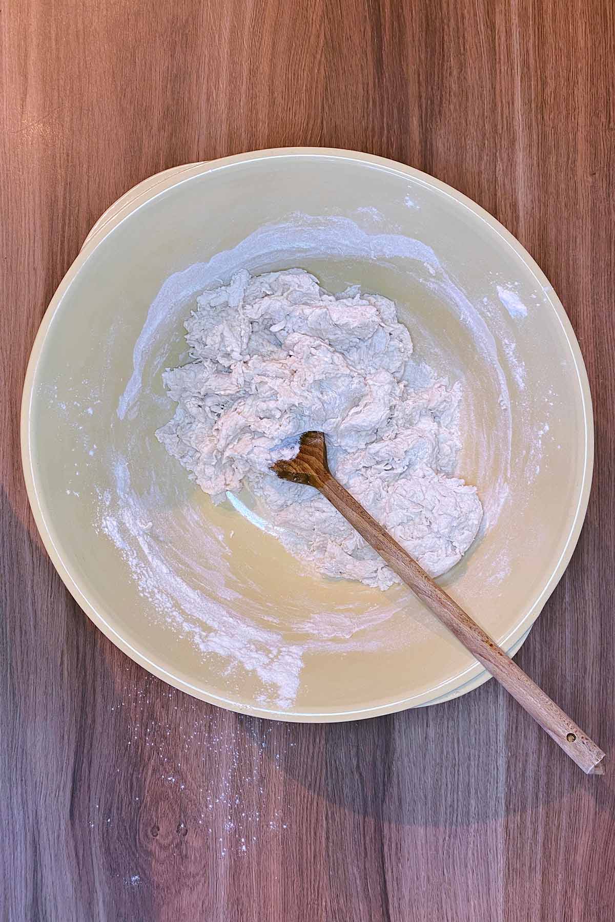 A sticky bread dough in a bowl with a wooden spoon.