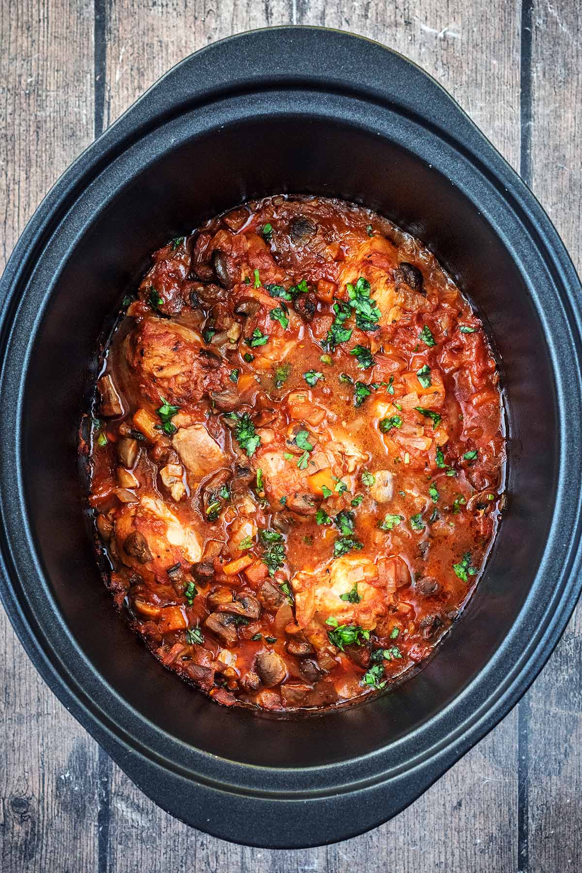 A slow cooker bowl containing cooked chicken chasseur.