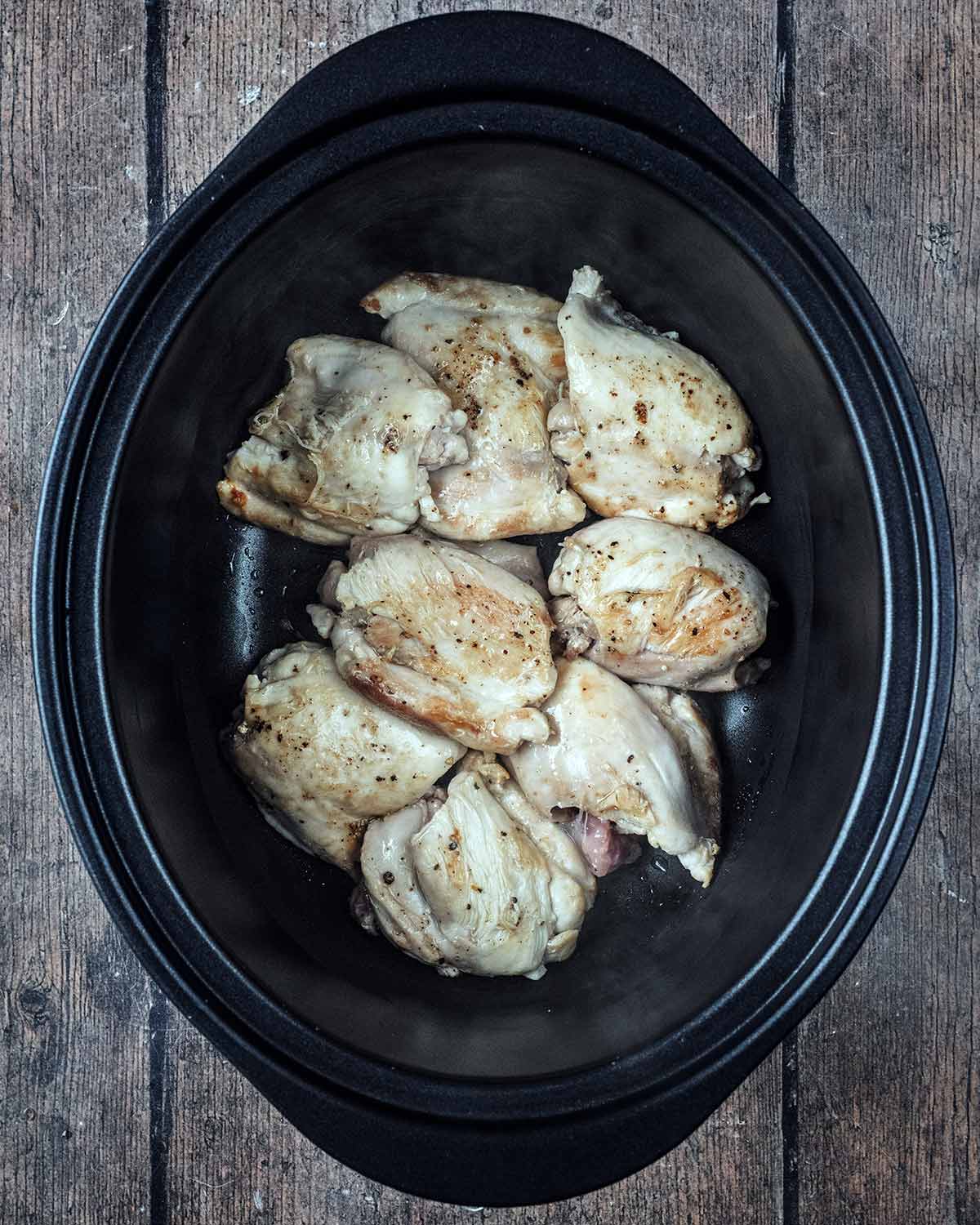 Browned chicken thighs in a slow cooker bowl.