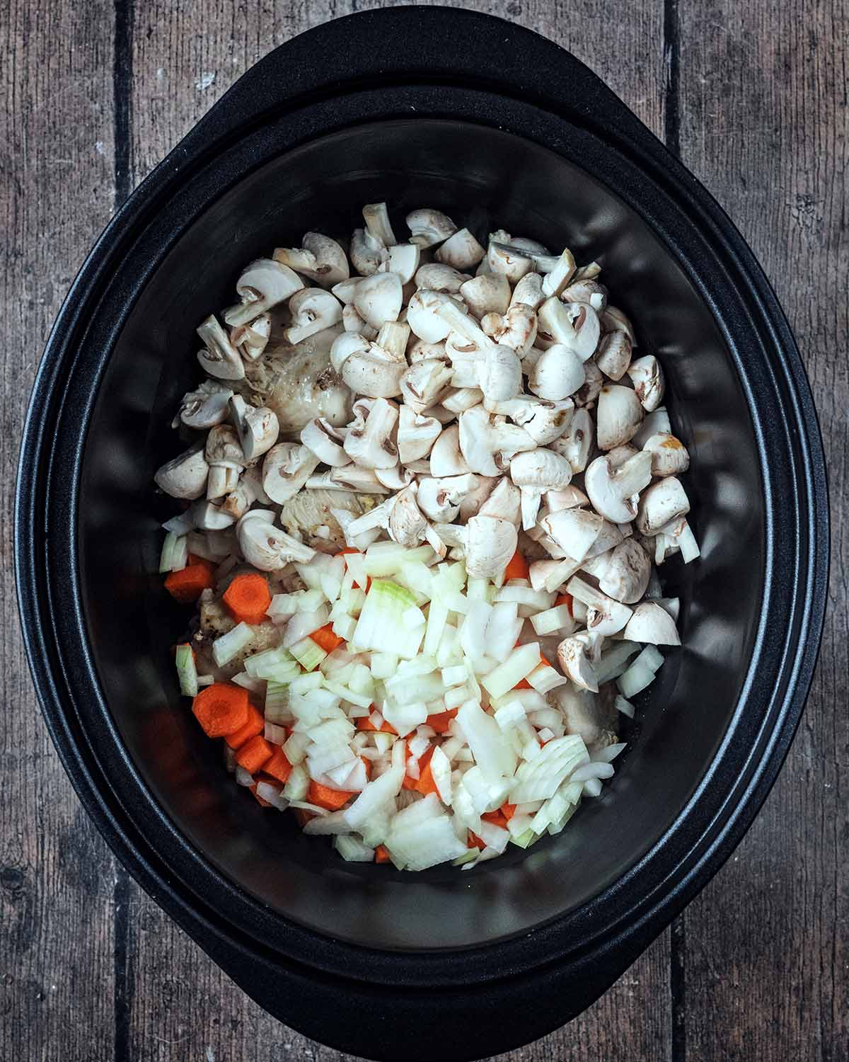 Chopped onions, mushrooms and carrots added to the slow cooker.