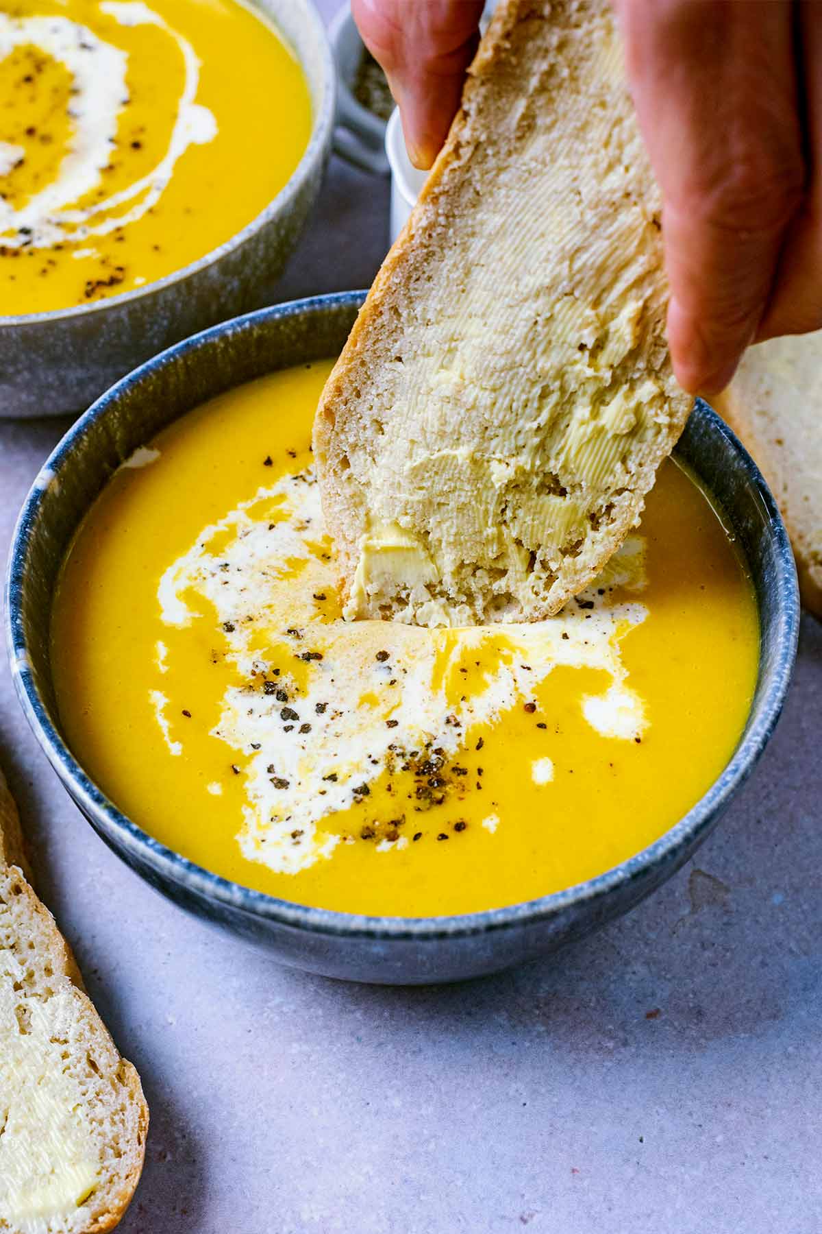 A slice of buttered bread being dipped into a bowl of soup.