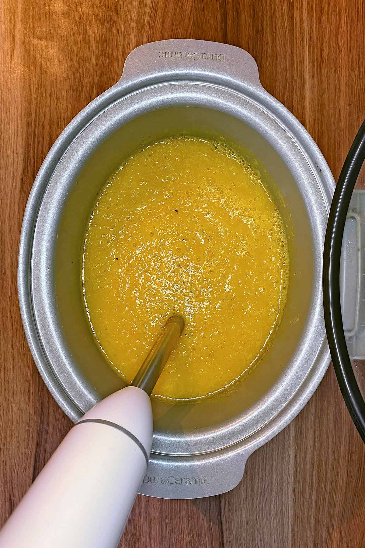An immersion blender blending soup in a slow cooker.