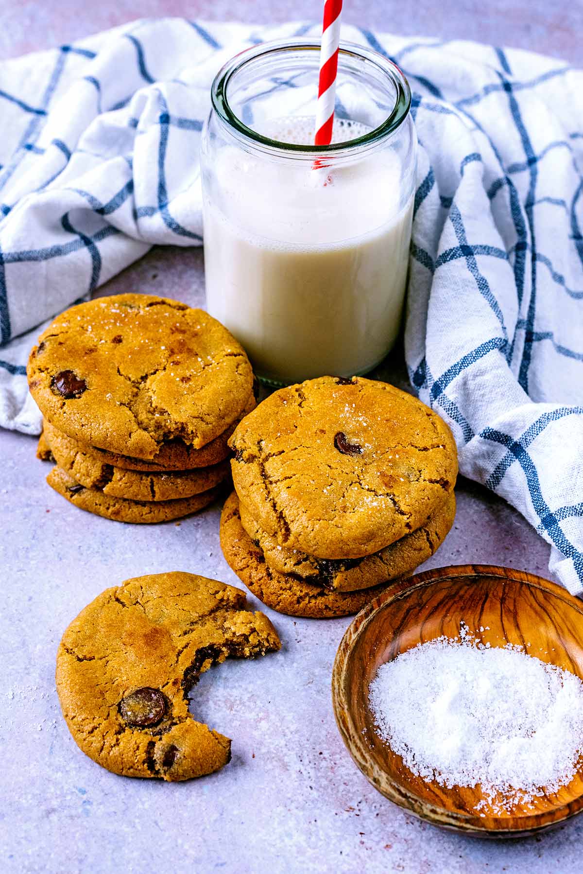Stacks of cookies and a cookie with a bite taken out. A glass of milk is next to them.