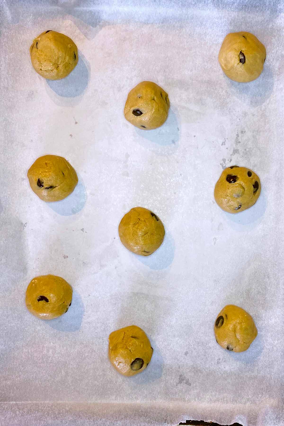 Nine balls of cookie dough on a lined baking sheet.