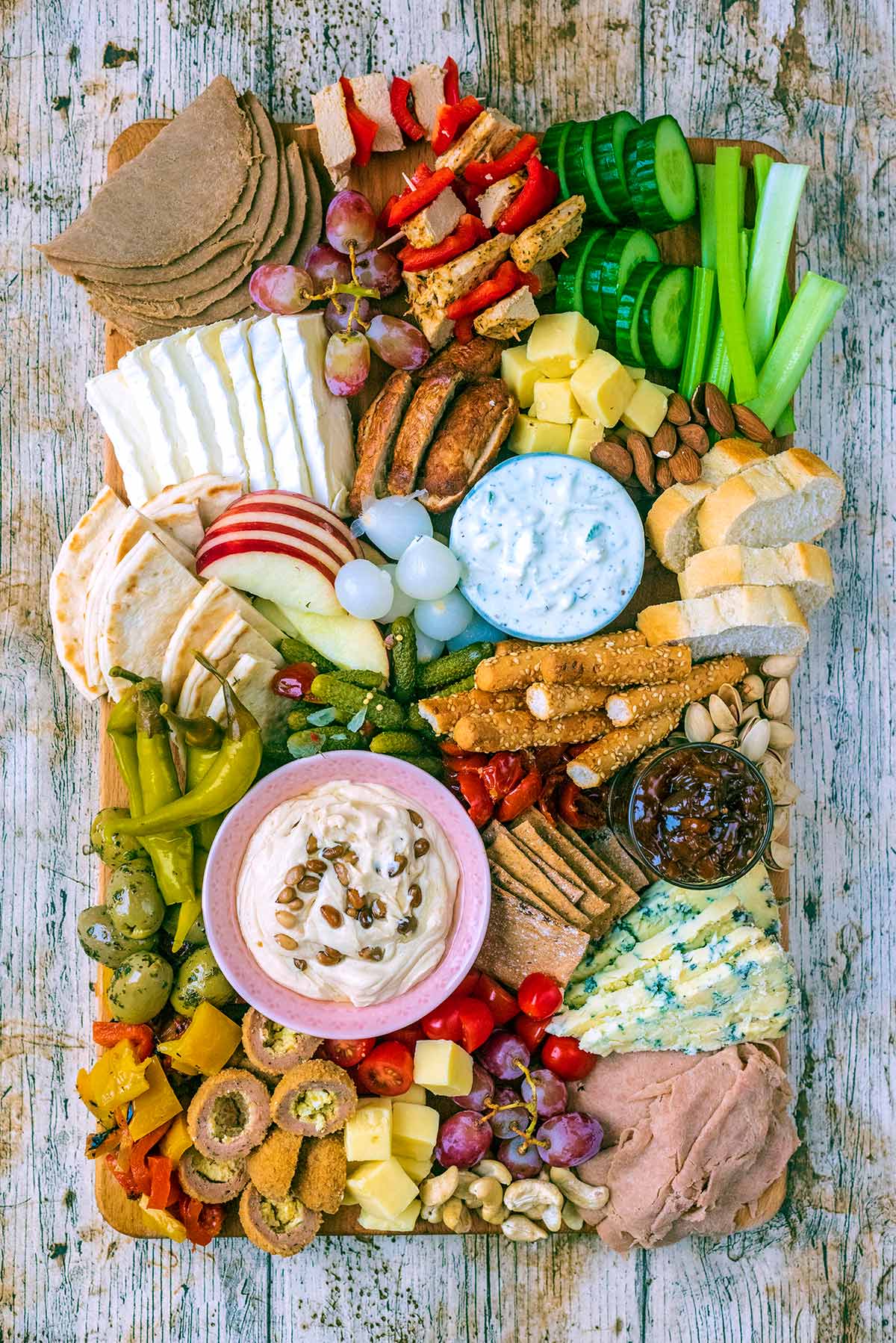 A charcuterie board full of meat, bread, cheese, nuts, pickles and vegetables.