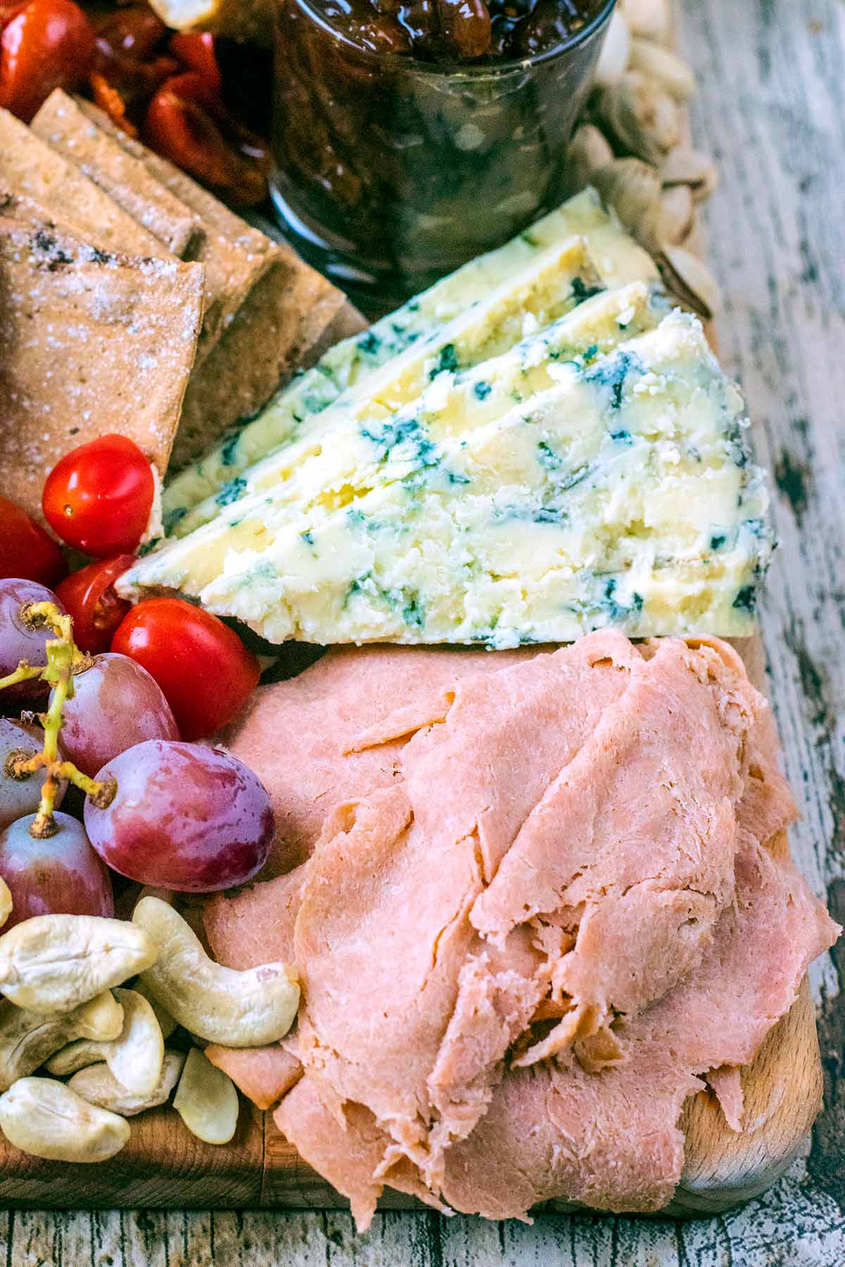 Some Quorn ham slices on a board with cheese, nuts, grapes and tomatoes.