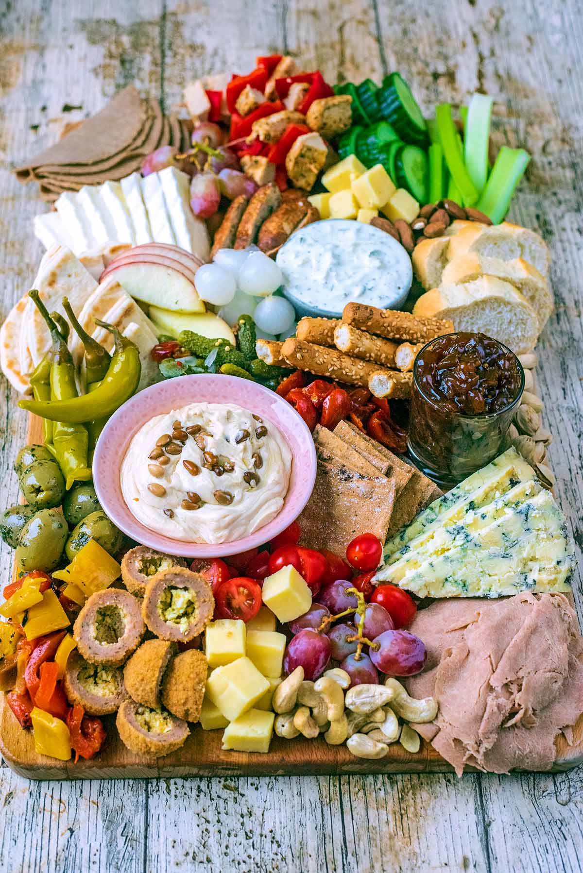 A charcuterie board containing meats, dips, cheeses, vegetables and bread.