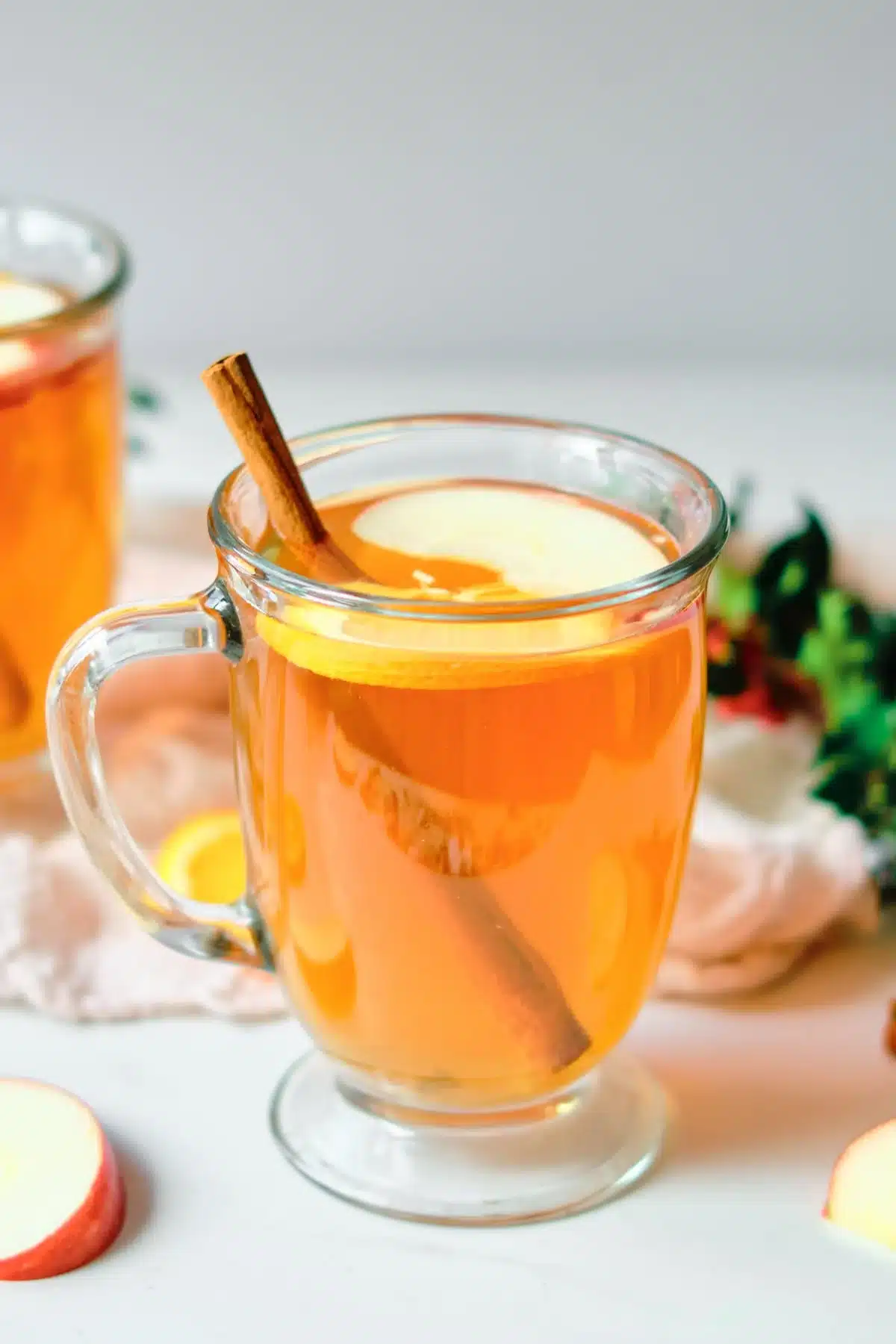 A glass of orange coloured tea with a lemon slice and a cinnamon stick.