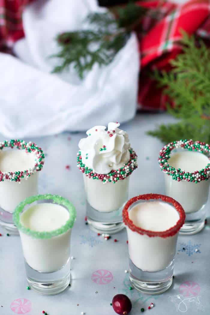 Five shot glasses containing a creamy drink decorated with red and green sprinkles.