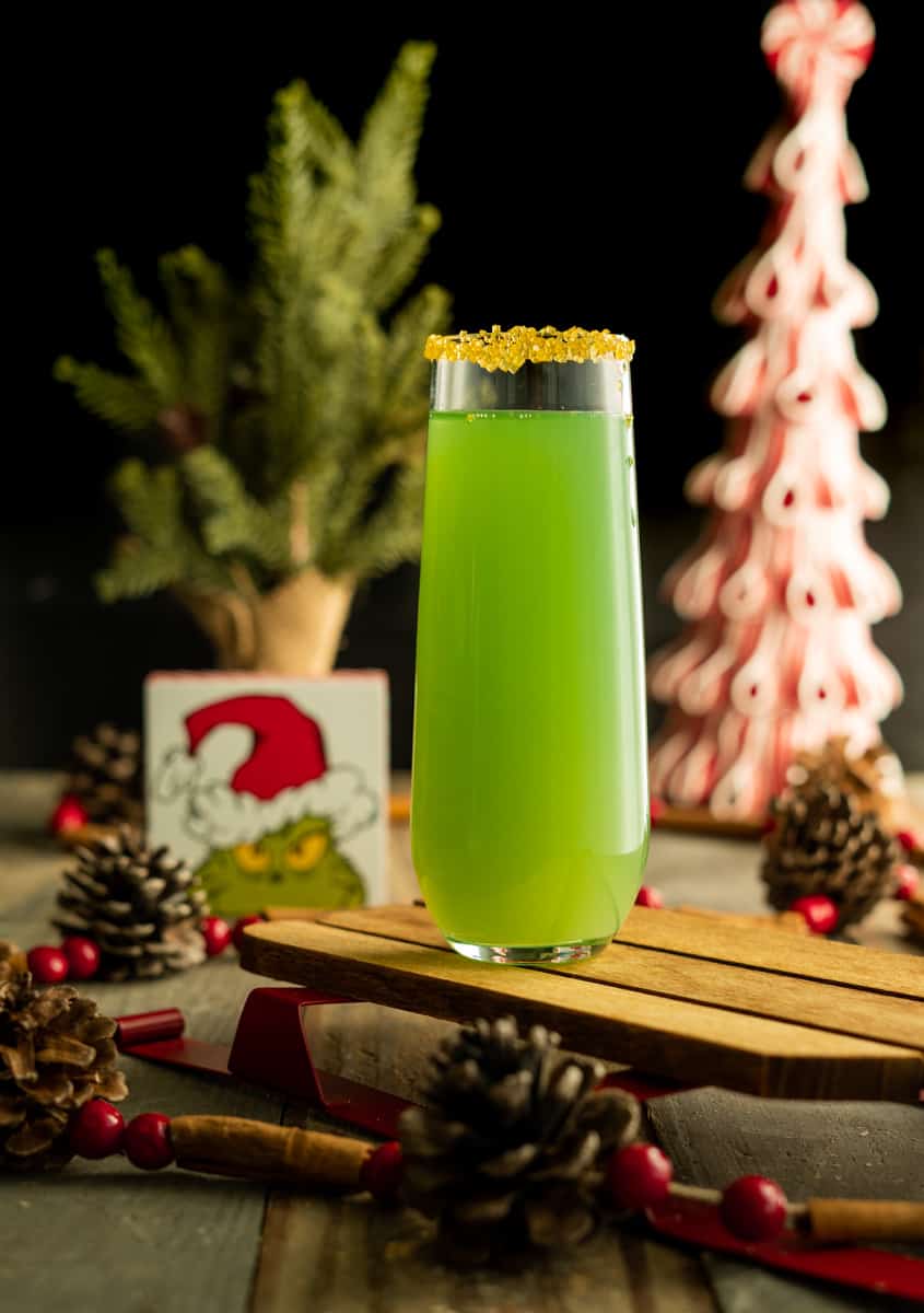 A tall glass filled with a vibrant green drink decorated with yellow sugar around the rim.