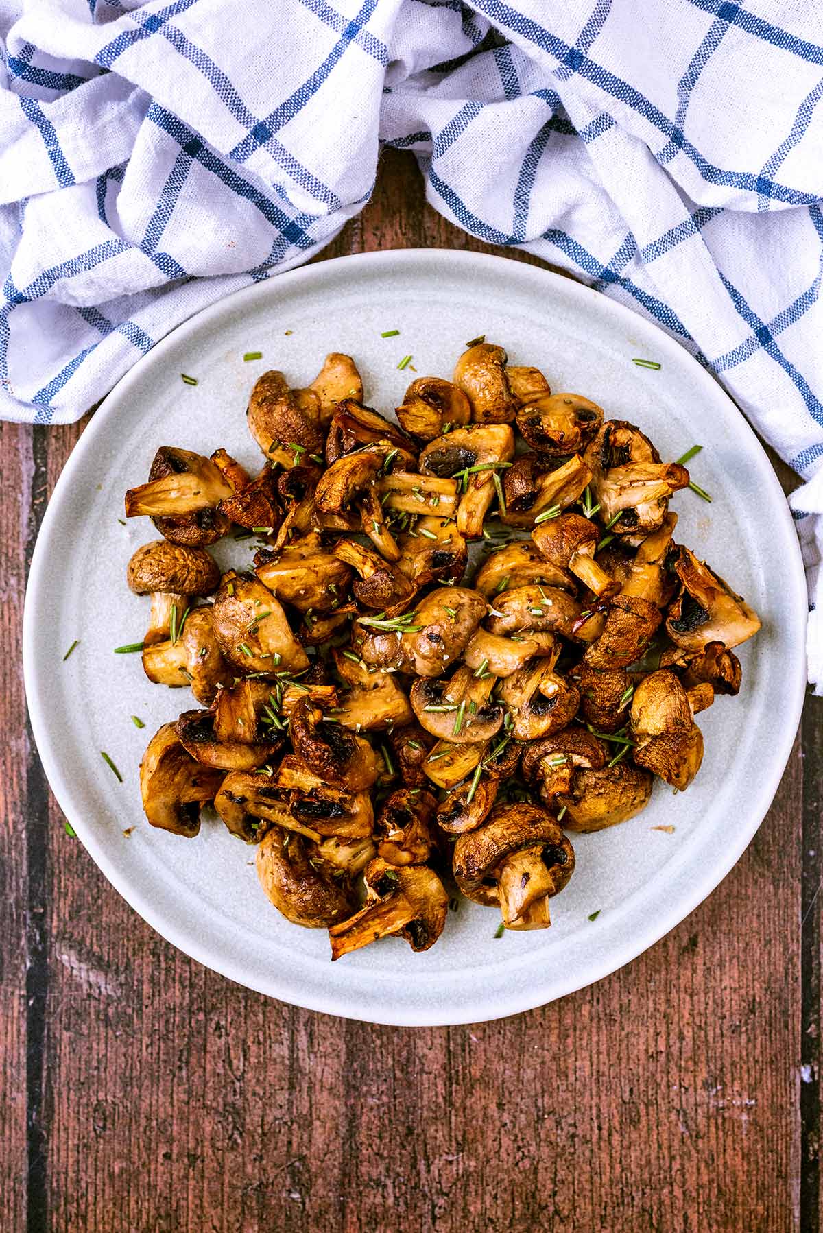 Cooked mushrooms on a plate next to a checked towel.