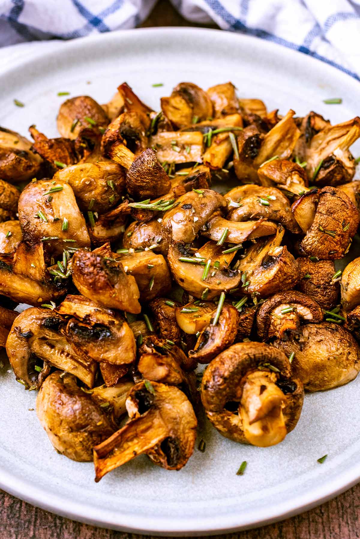 A plate of cooked mushrooms in front of a tea towel.