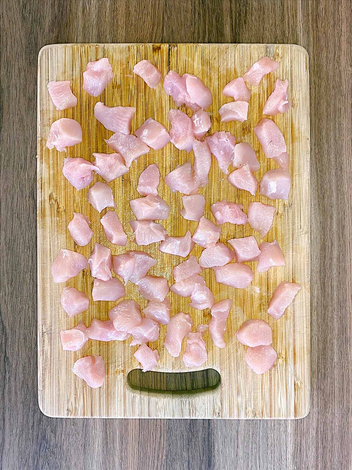 Small cubes of diced chicken on a wooden chopping board.