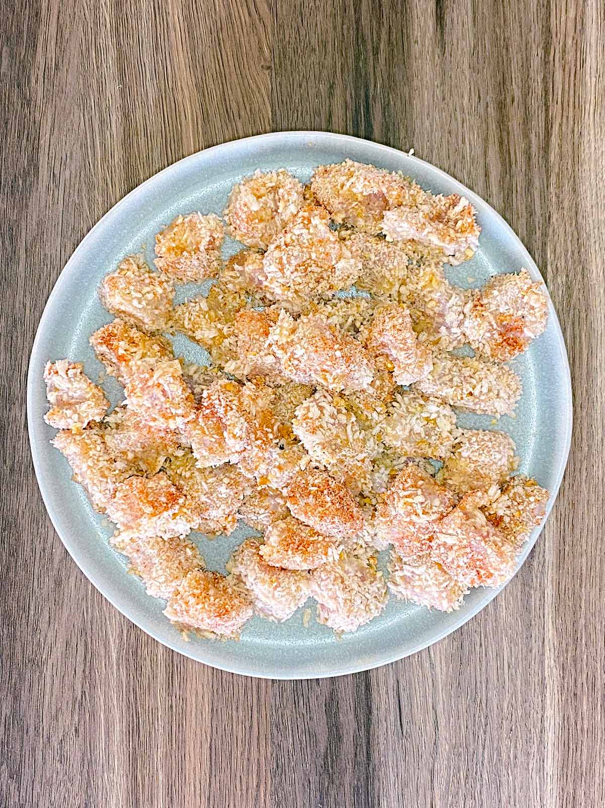 A plate of breaded, raw chicken cubes.