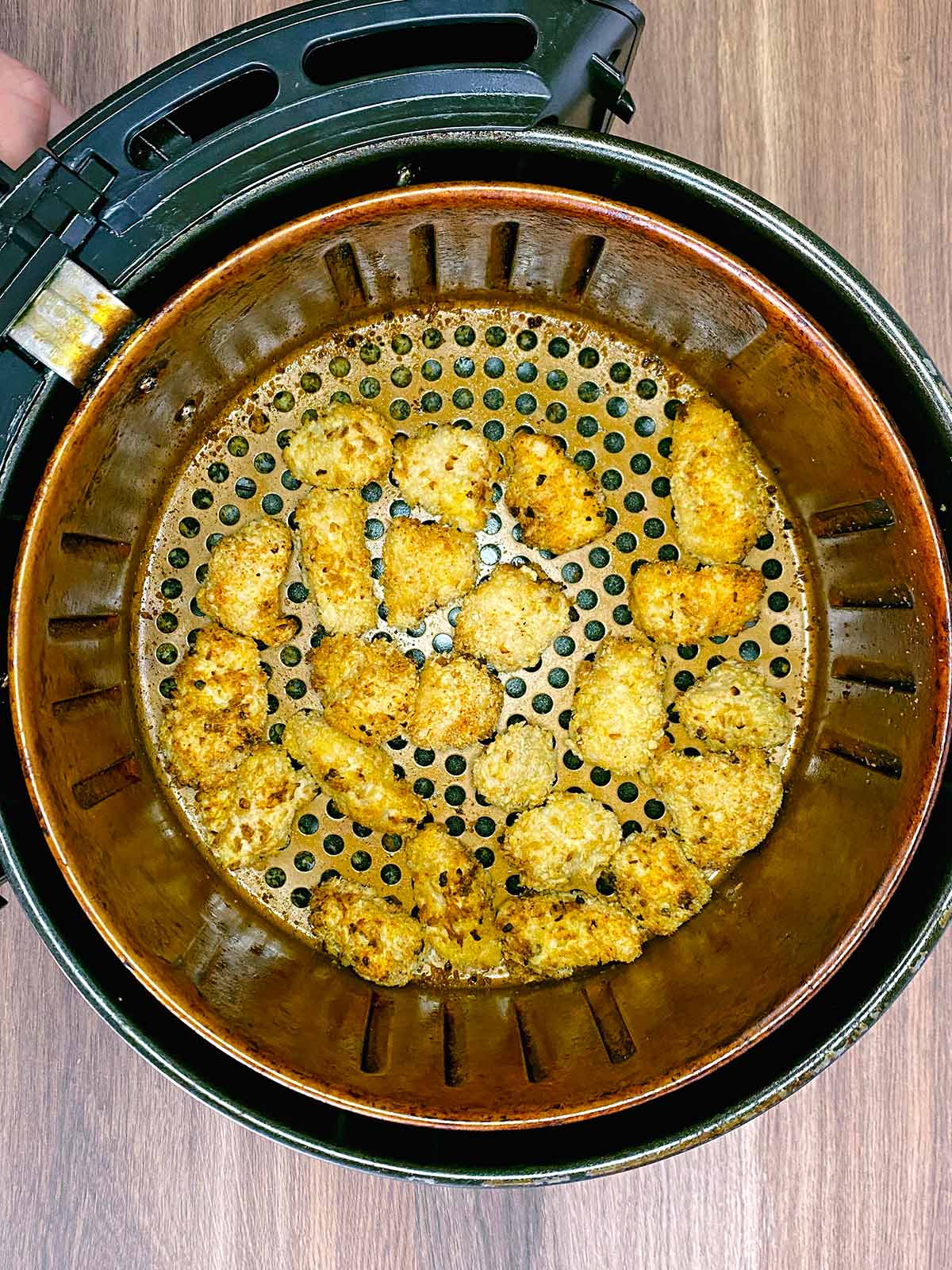 Cooked popcorn chicken in an air fryer basket.