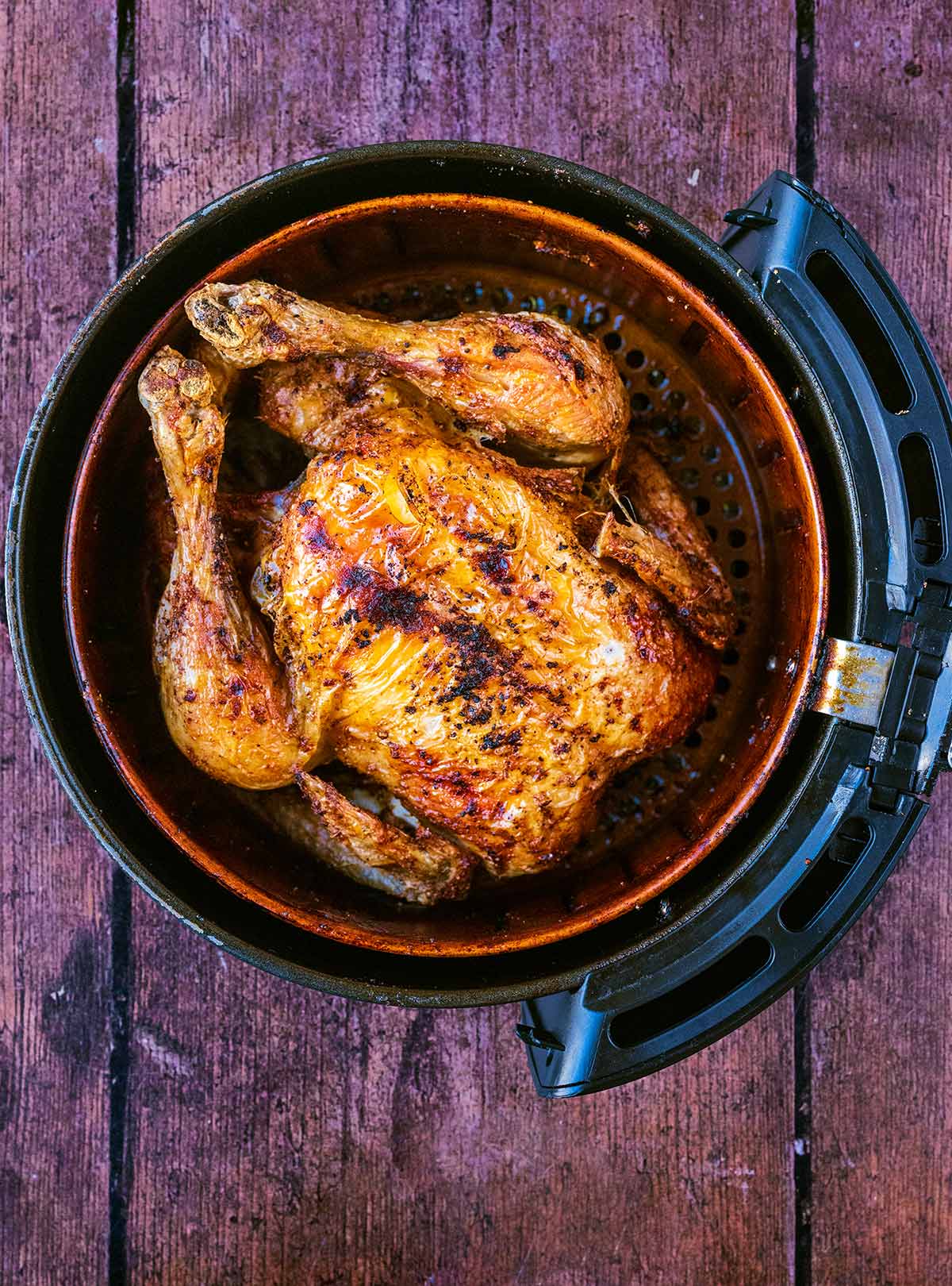 A cooked whole chicken in an air fryer basket.