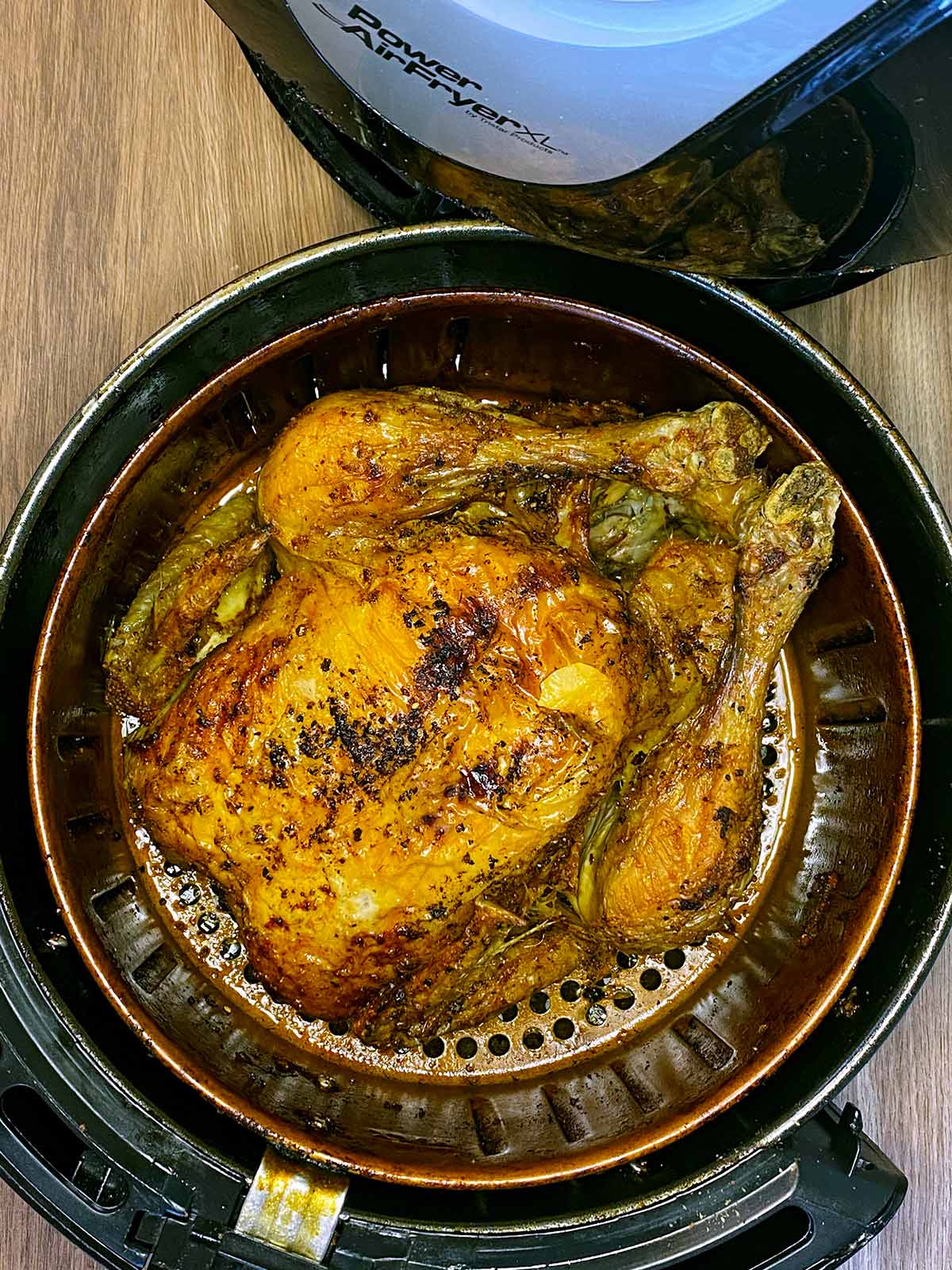 Cooked whole chicken in an air fryer basket.