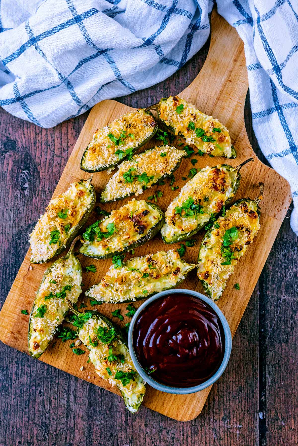 Jalapeno poppers on a serving board with a pot of barbecue sauce.