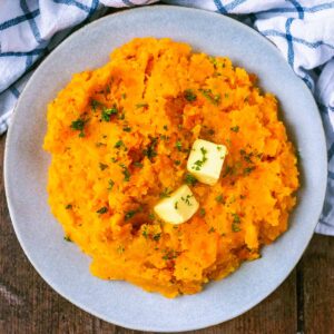 Carrot and swede mash on a plate topped with two pats of butter.