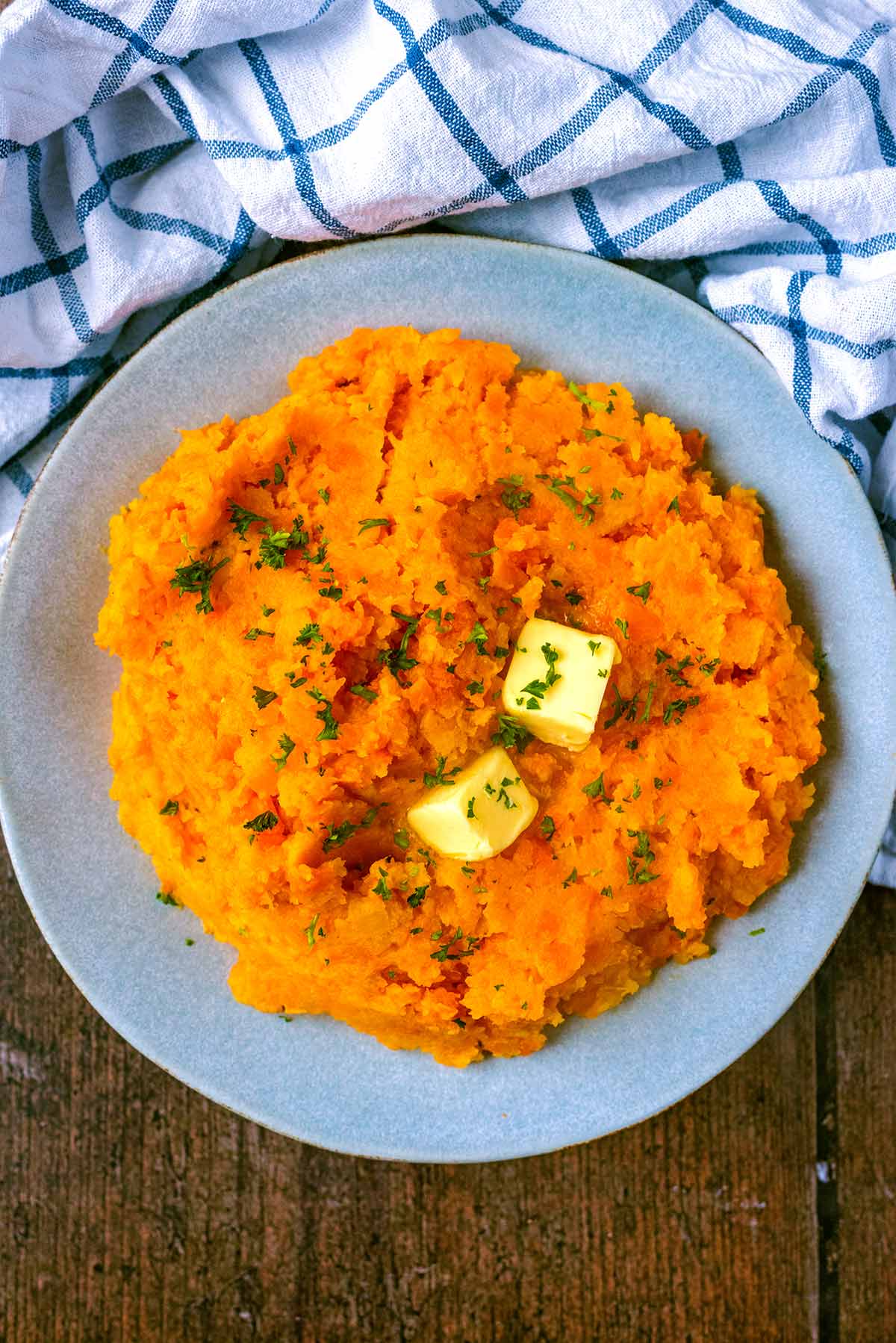 A plate of orange coloured mash topped with butter and chopped herbs.