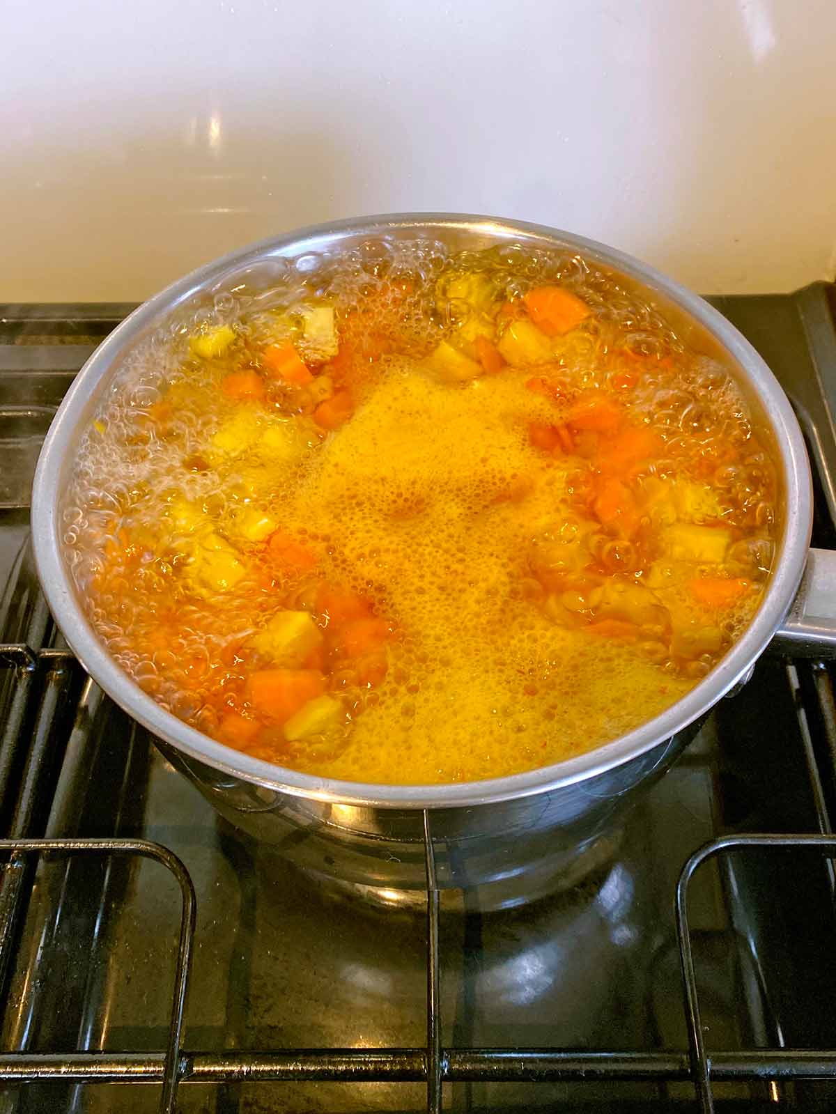 Chopped carrot and swede boiling in a pan on a hob.