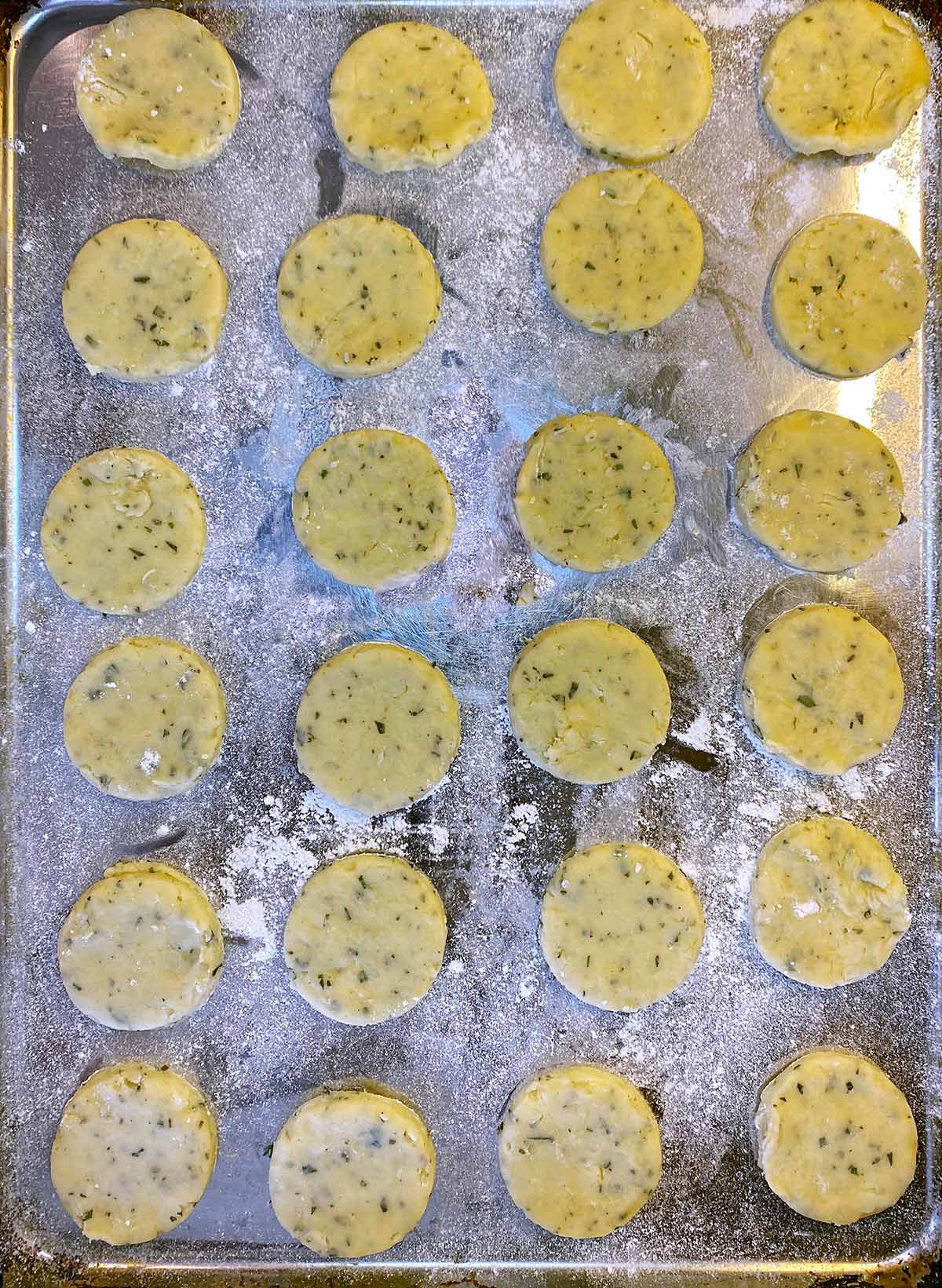 Twenty four uncooked biscuits on a floured baking tray.
