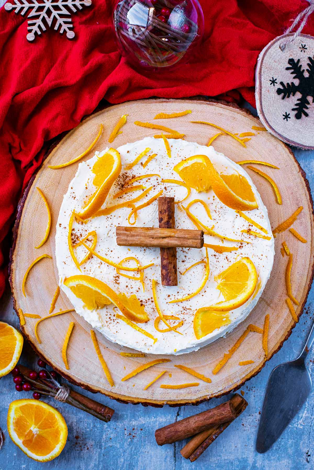 A cheesecake on a wooden board topped with cinnamon sticks and orange slices.