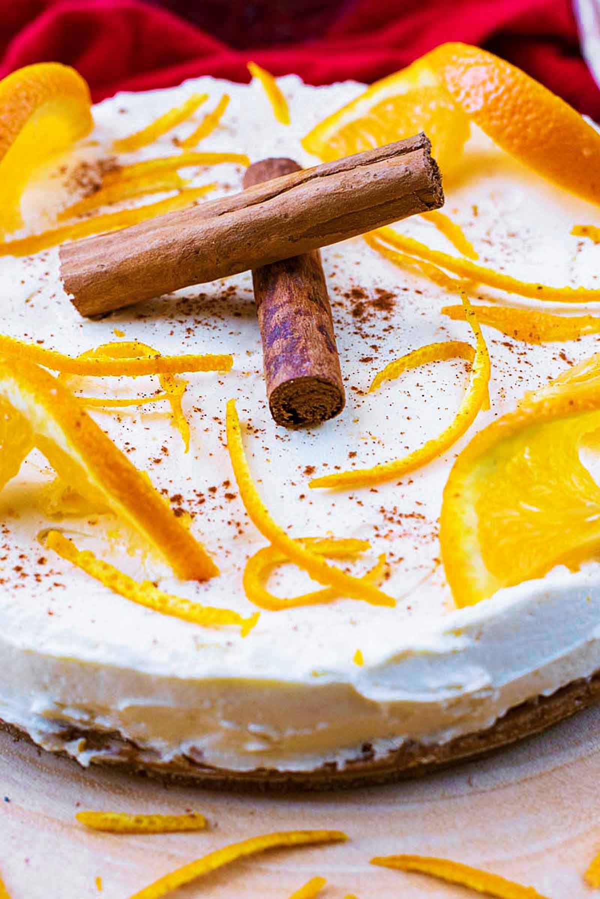 A cheesecake with orange slices, orange peel and two cinnamon sticks on top.