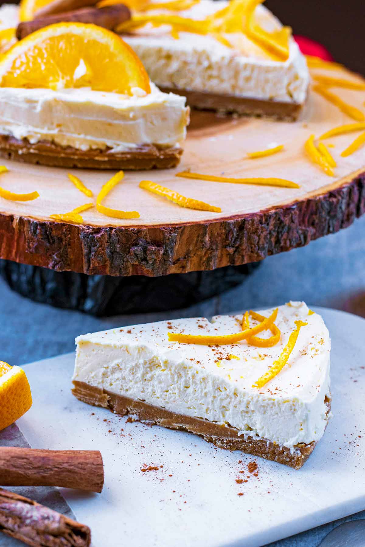 A slice of cheesecake on a serving board with the rest of the cheesecake in the background.