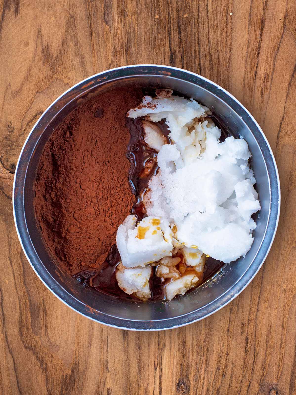 A saucepan containing coconut oil, cocoa powder and maple syrup.