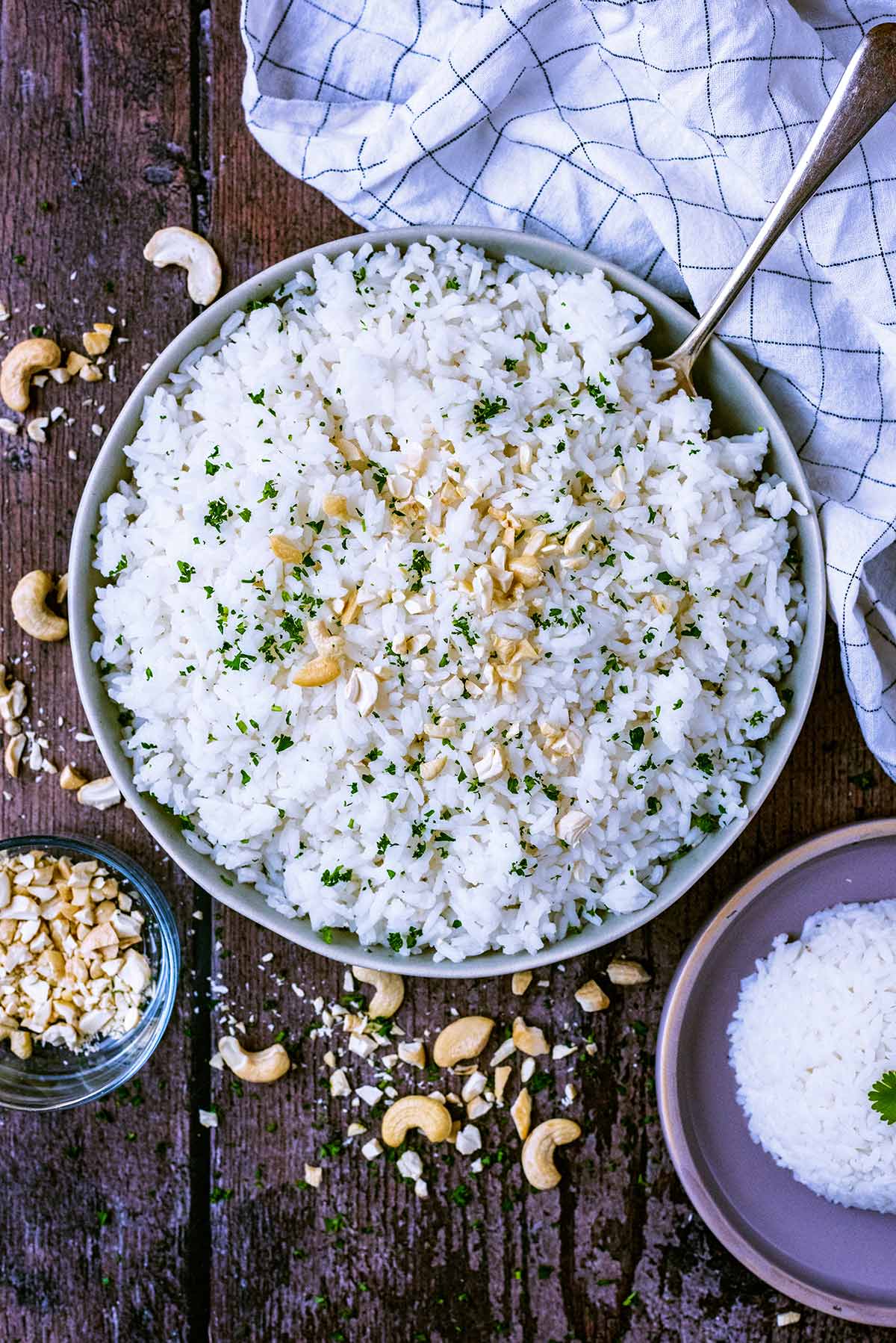 A large bowl of rice with a spoon, next to a towel and some crushed cashews.