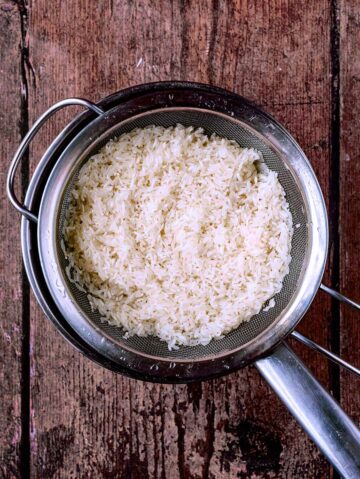A sieve containing rinsed rice over a saucepan.
