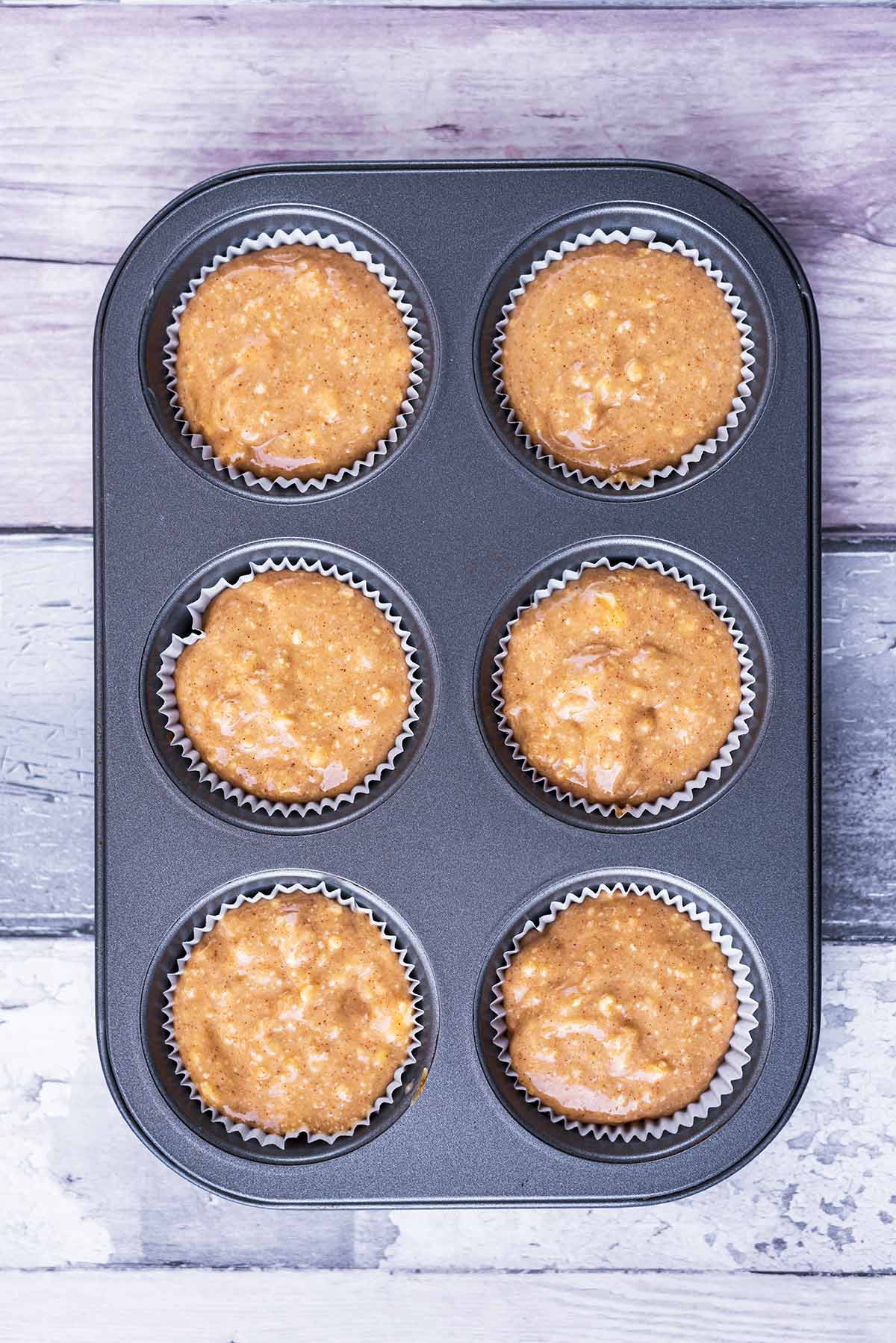 A six hole cupcake tin with cake batter in each hole.