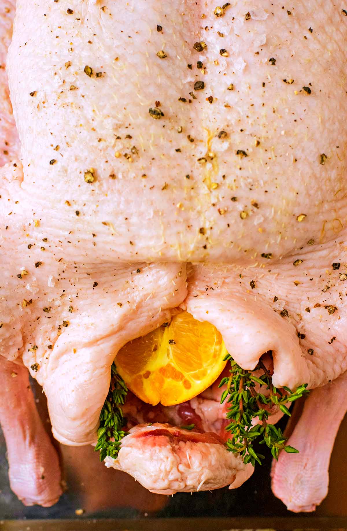 An uncooked duck in a roasting pan. An orange half and thyme are in the bird's cavity.