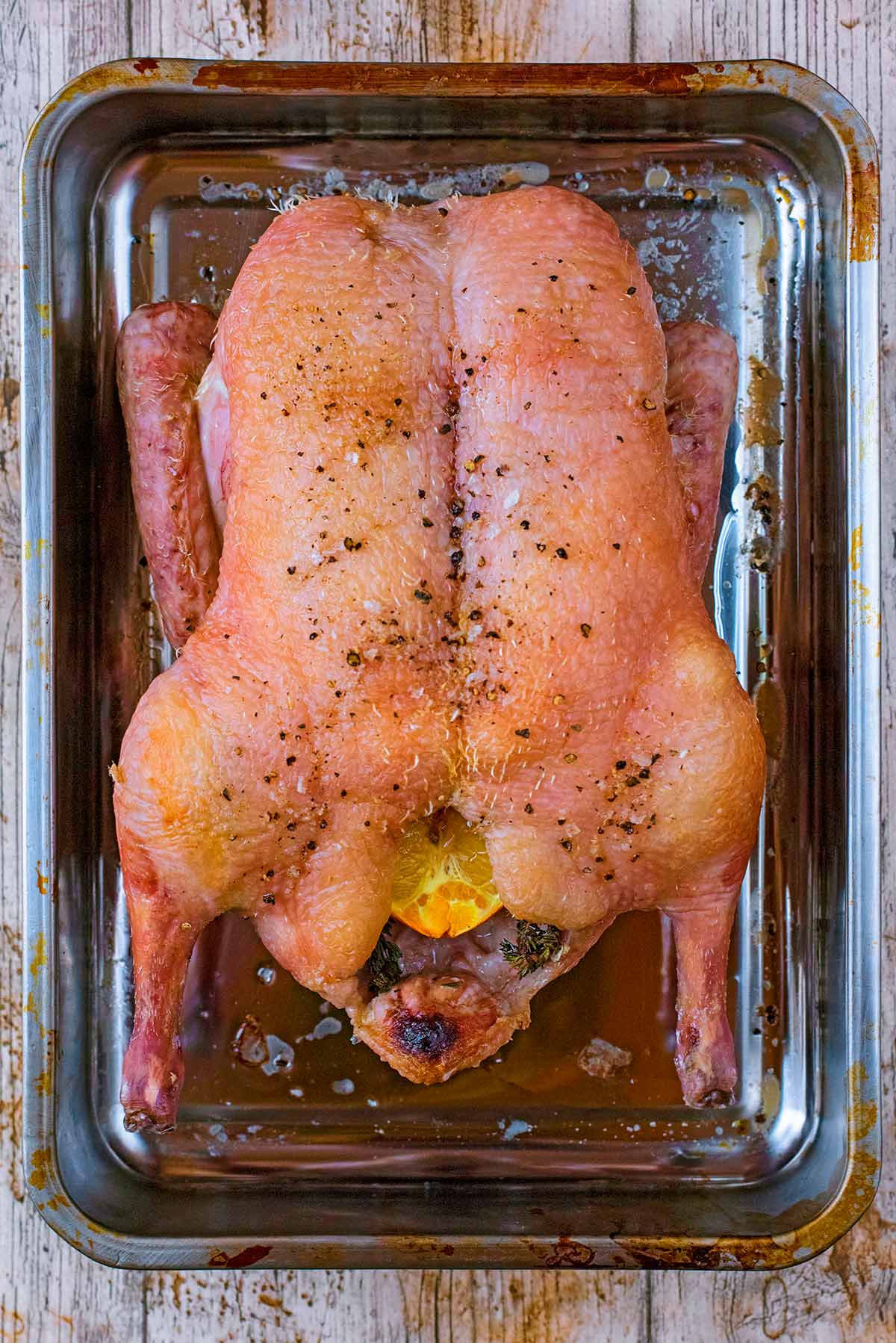 A whole, partly cooked, duck in a roasting pan.