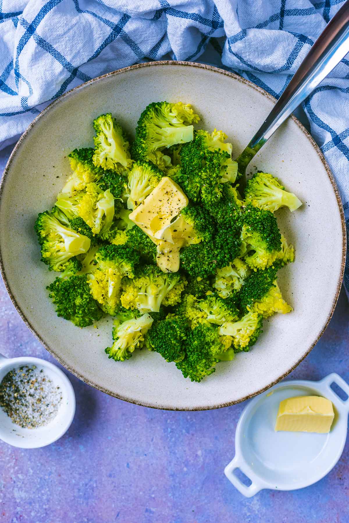 A bowl of cooked broccoli florets with butter melting over it.