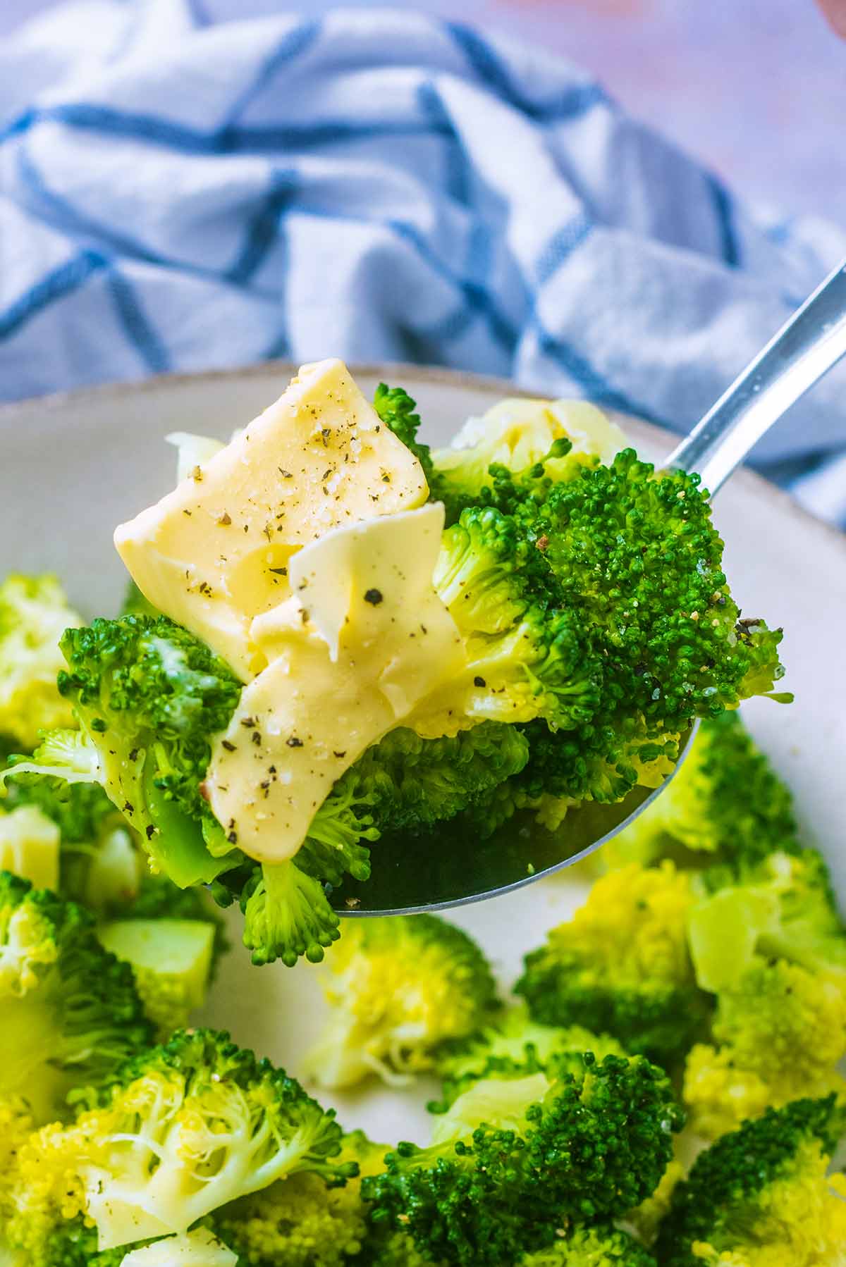 A spoon lifting up come cooked brocoli and some melting butter.