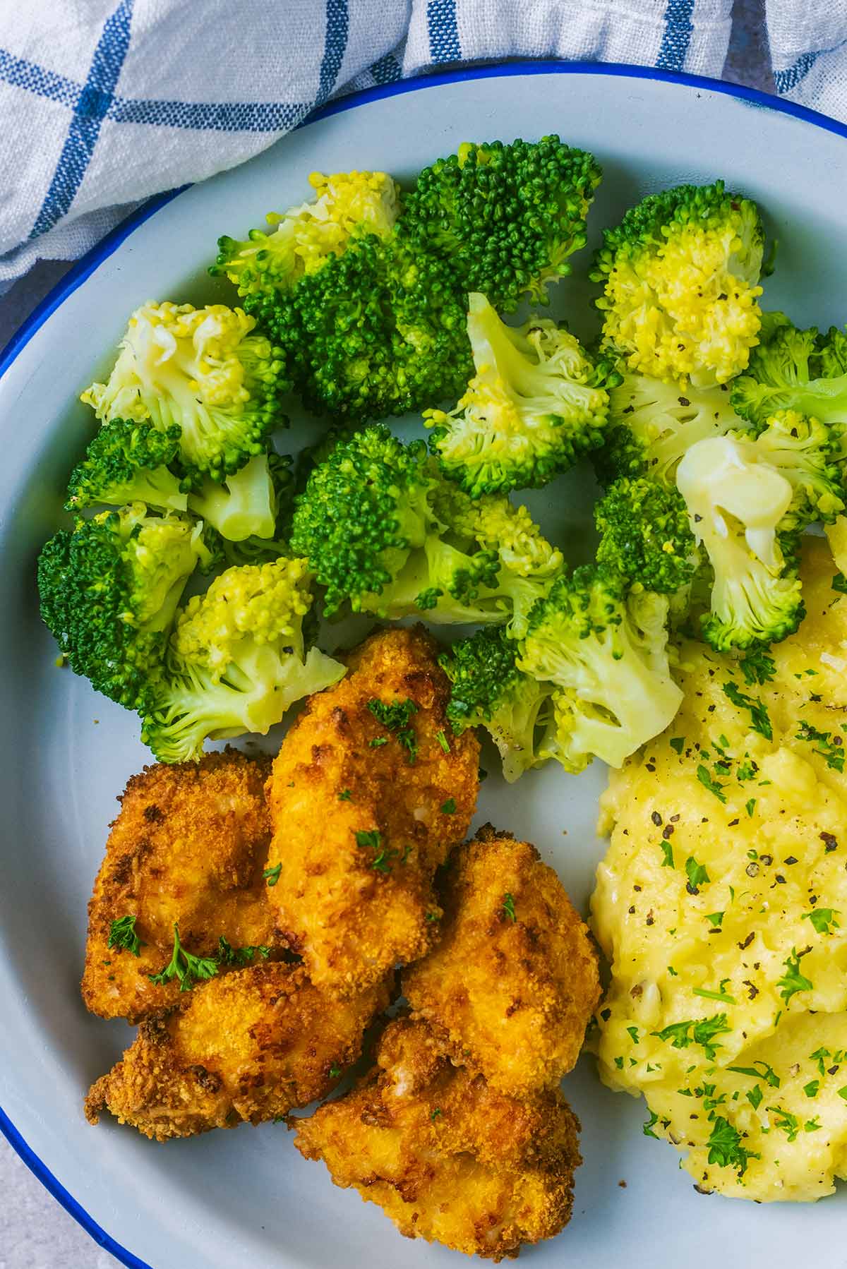 A plate of cooked broccoli, mashed potato and chicken nuggets.