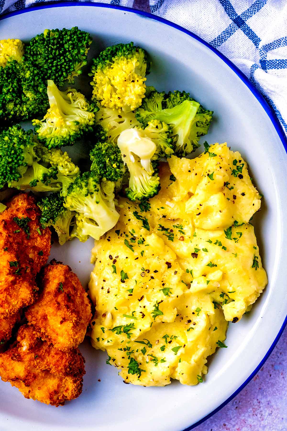 Mashed potato on a plate with broccoli and chicken nuggets.