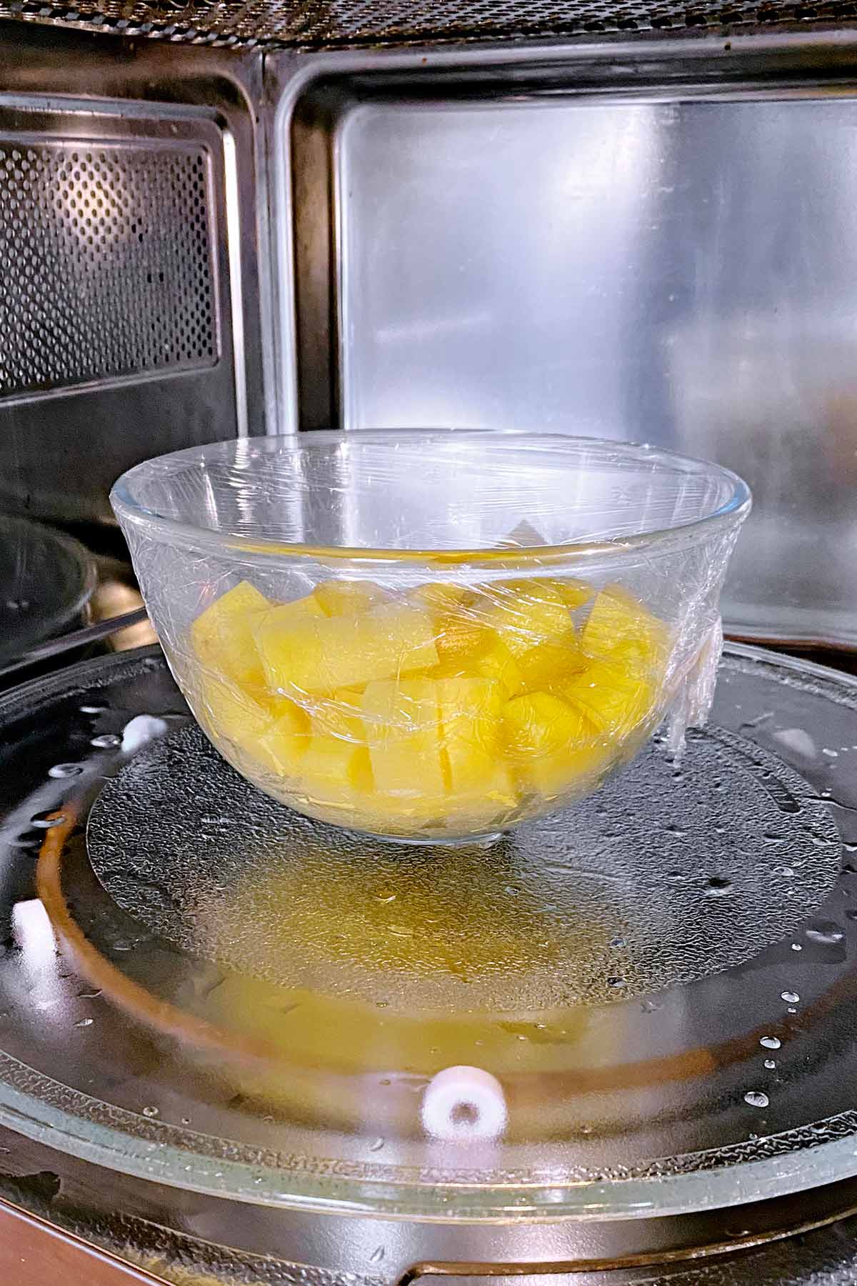 A glass bowl of potatoes in a microwave.