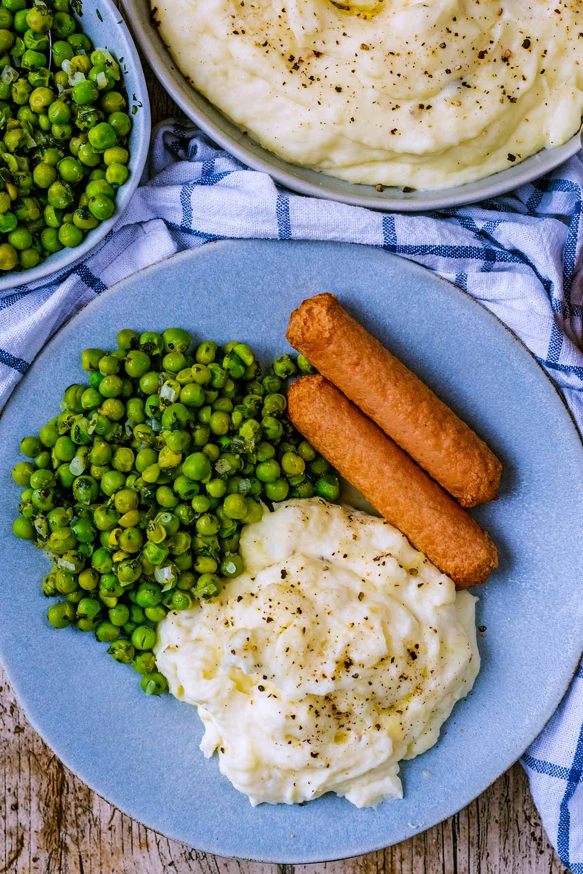 A plate with sausages, mashed potato and peas on it.