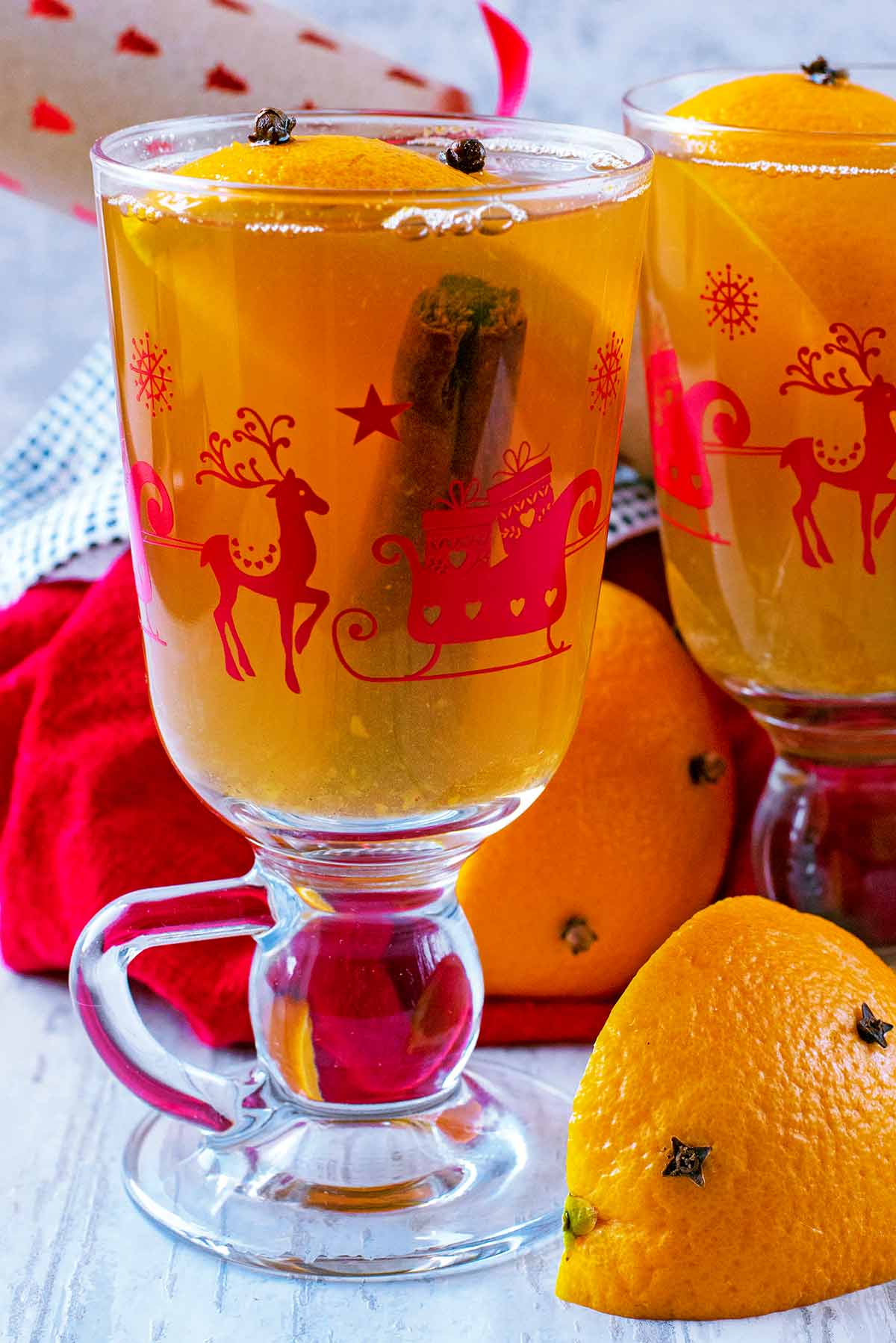 A cinnamon stick and orange segment in juice in a Christmas glass.