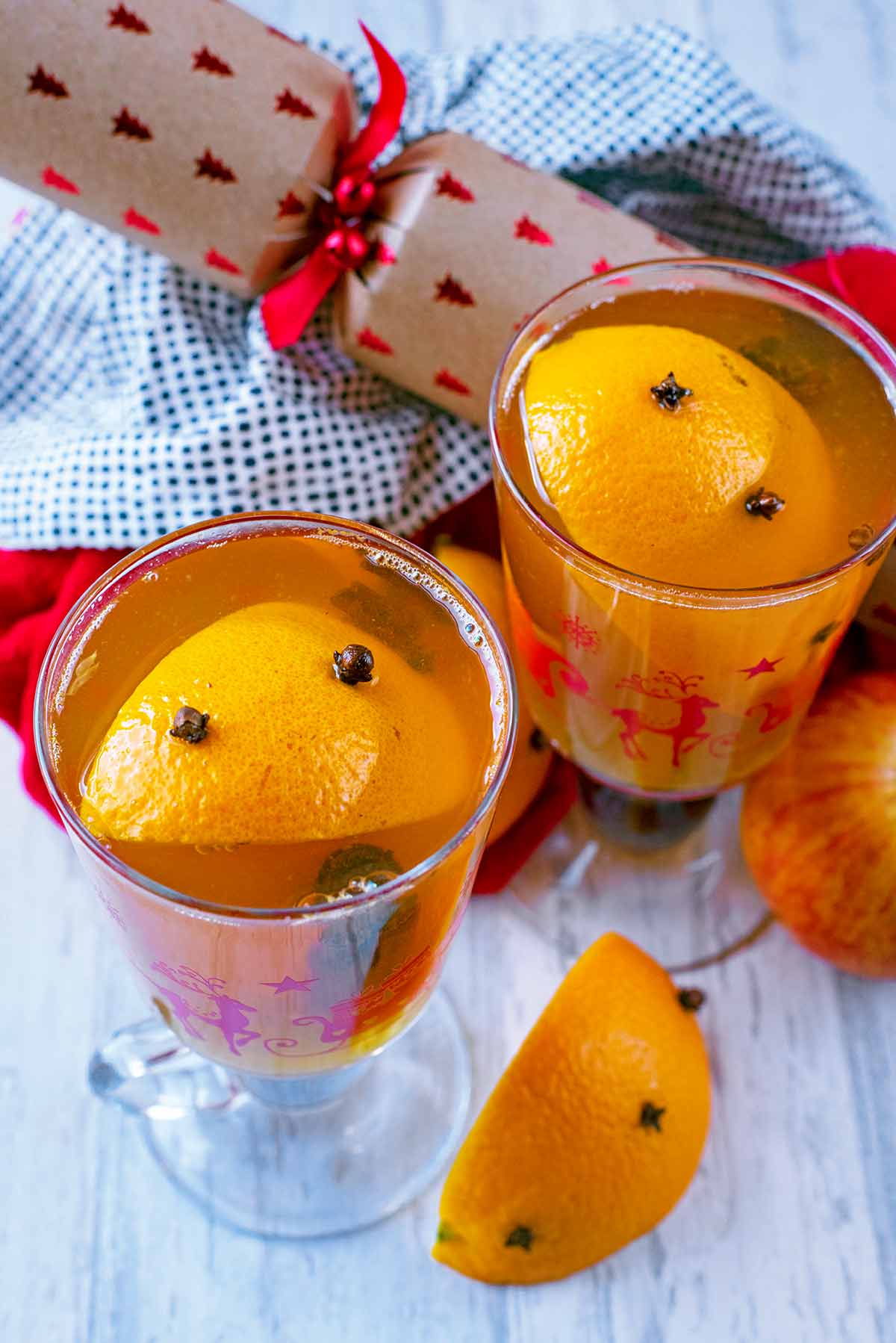 Clove spiked oranges floating in two glasses of Mulled Apple Juice.