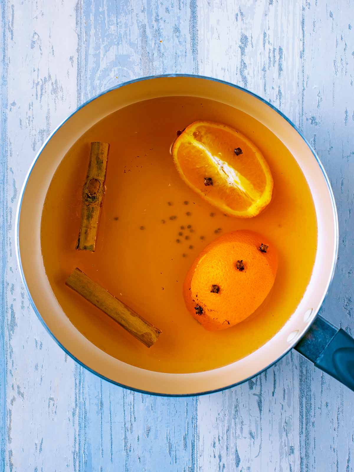 Clove studded orange quarters added to the pan.