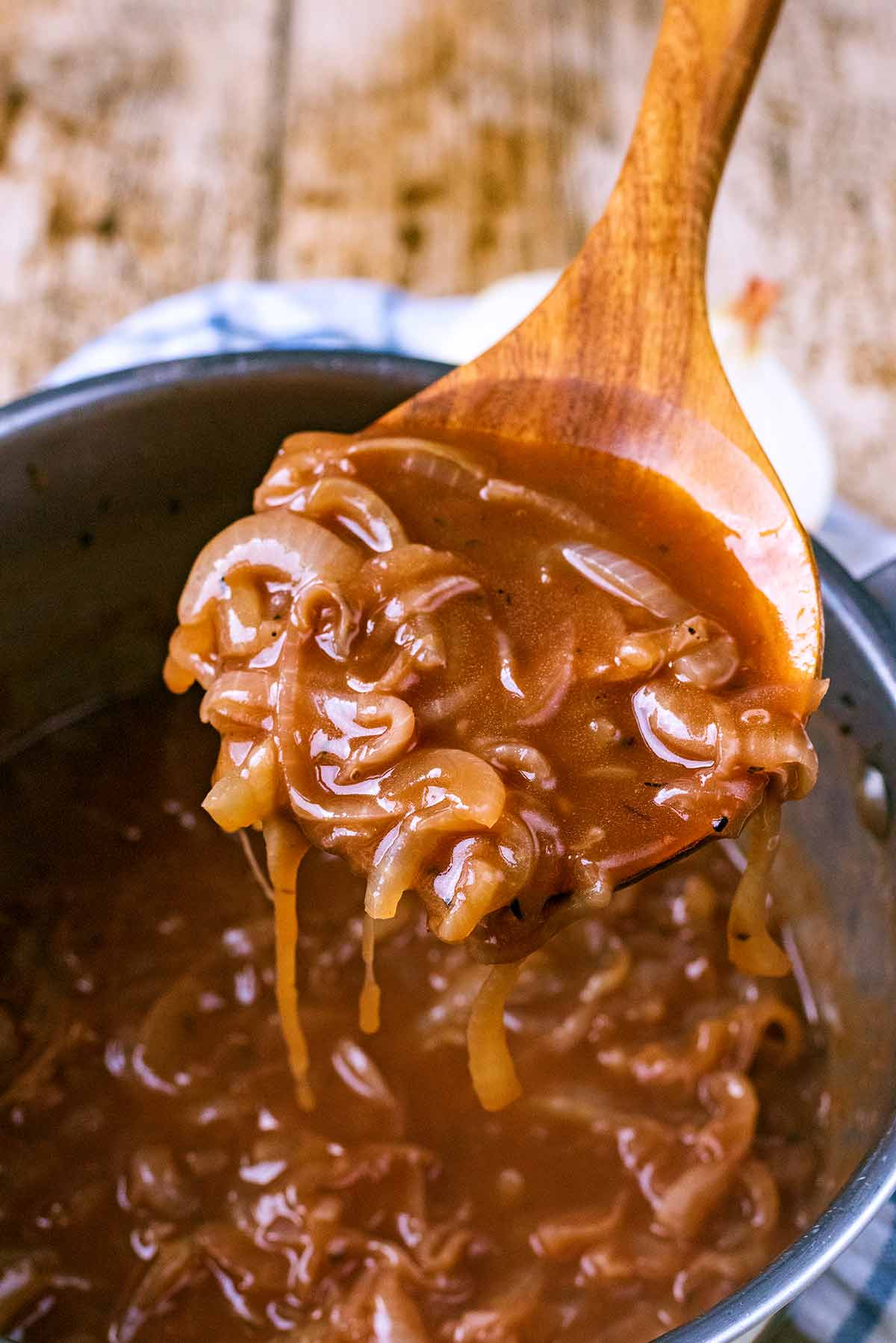A wooden spoon lifting some onion gravy out of a pan.