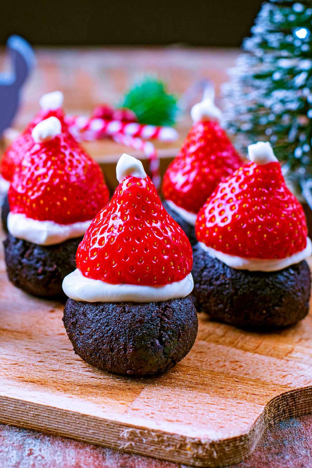 Strawberry topped brownies on a wooden serving board with Christmas decorations in the background.