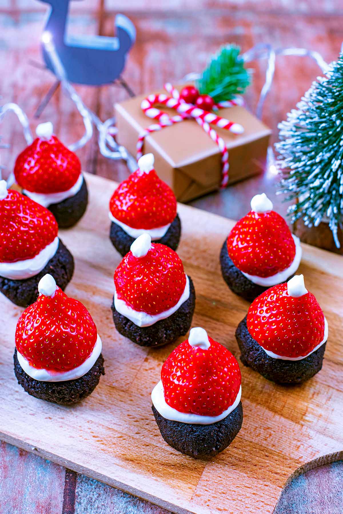 Santa Hat Brownies on a wooden serving board with Christmas decorations in the background.