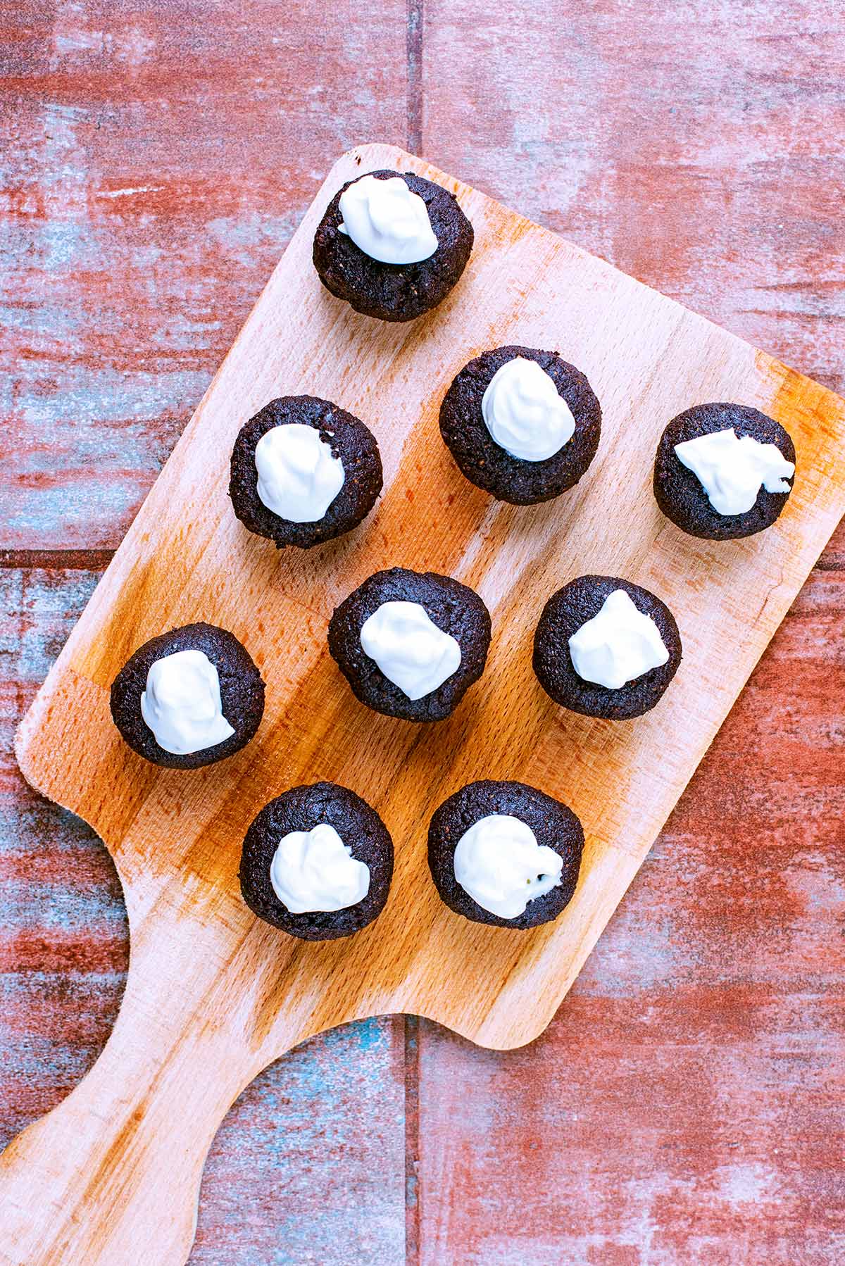 Nine raw brownie balls, all topped with yogurt, on a wooden board.